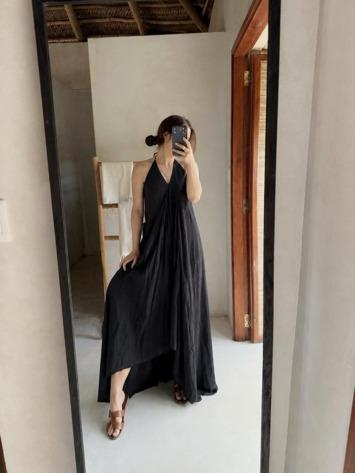 A woman takes a mirror selfie wearing the Flamingo Maxi Dress in solid black, plunging V-neckline and high-low hem