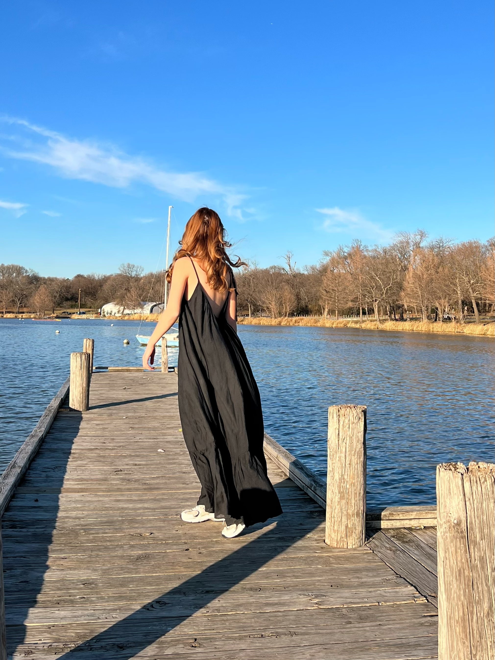 Woman in a hand-dyed black backless maxi dress standing by the sea, wearing boho resortwear by Coco de Chom