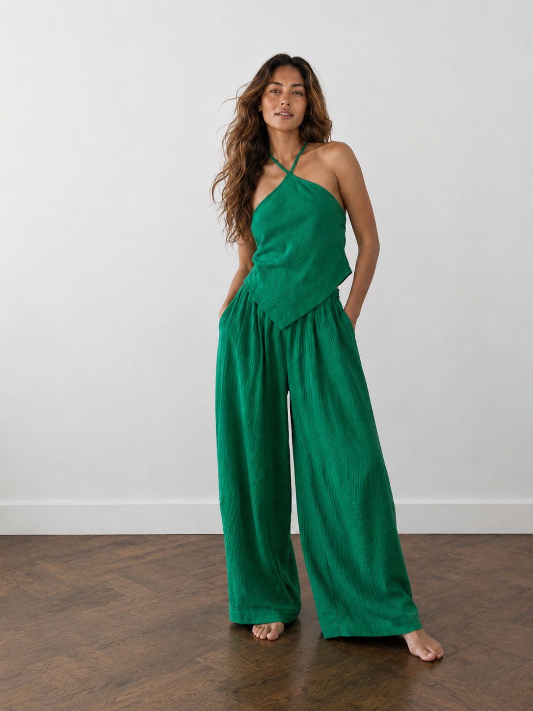 Woman wearing an emerald green handkerchief halter top and matching wide leg pants, boho vacation outfit and resort wear set for beach travel