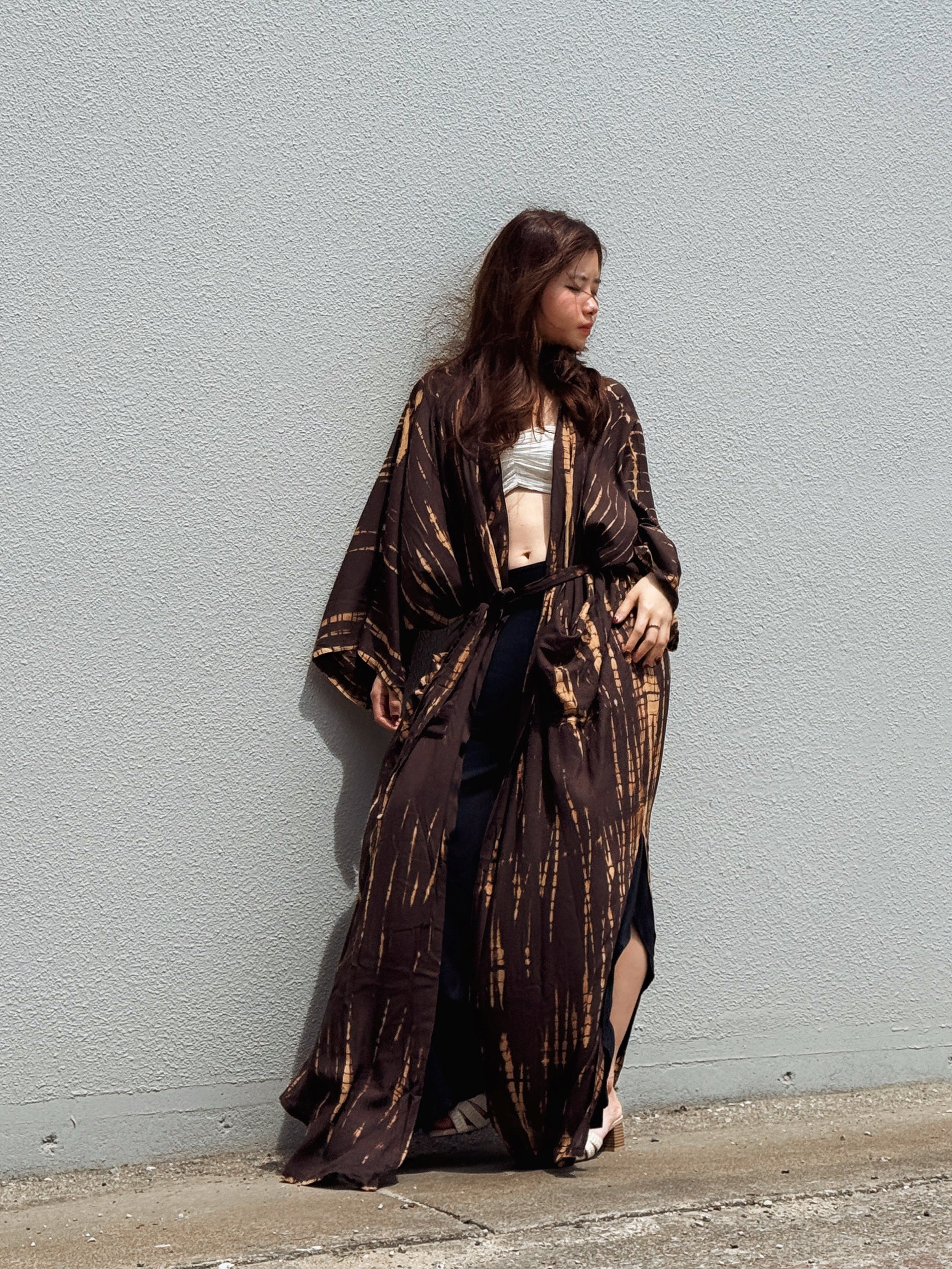 Woman wearing a handmade long tie-dye kimono robe in brown with long sleeves and adjustable waist tie, styled as a boho duster and lightweight beach cover-up by Coco de Chom.