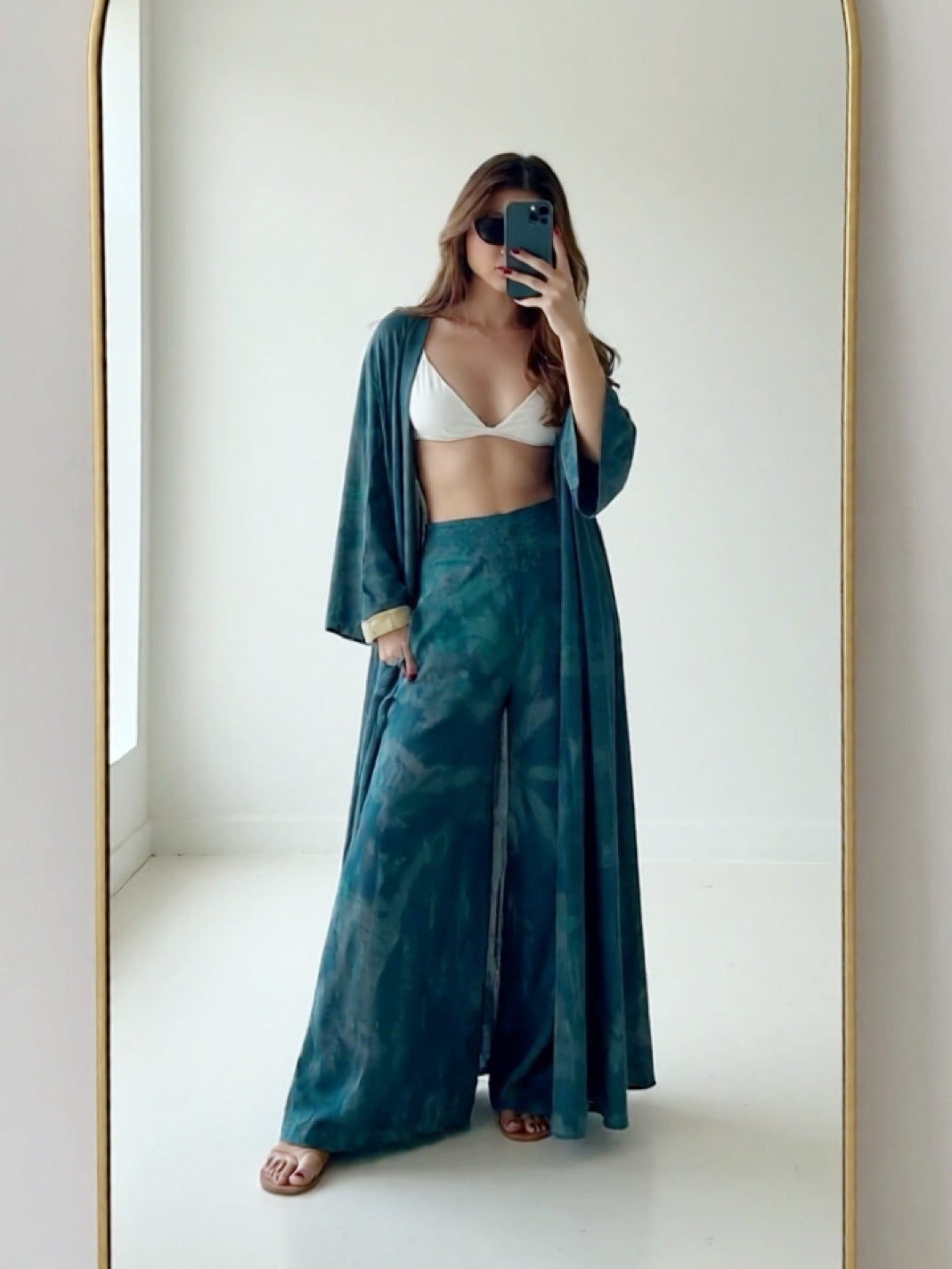 Woman wearing a teal tie dye kimono beach outfit with a white top in front of a mirror.