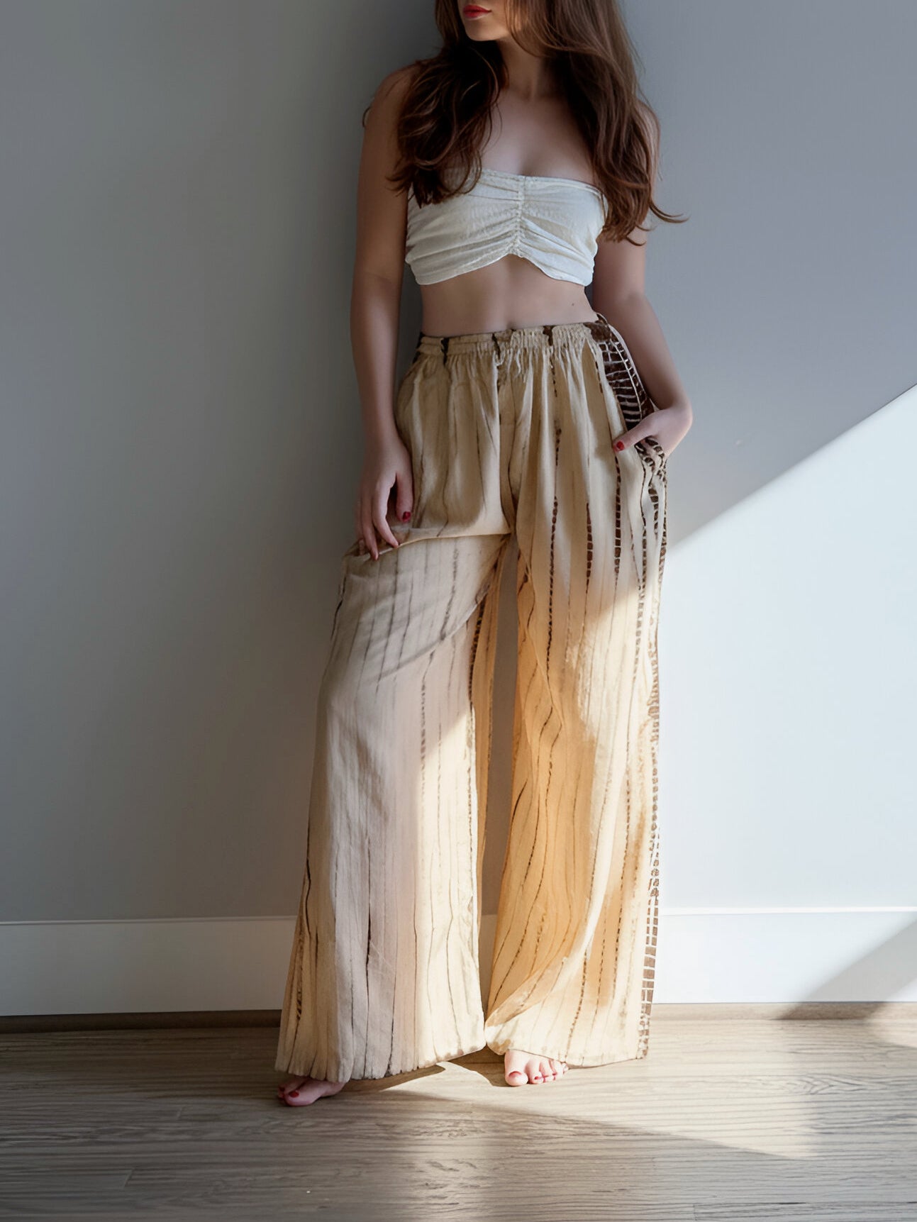 Woman wearing a white top and beige tie dye wide-leg pants, giving a look boho vibe perfect outfit for beach vacation, standing in a room with sunlight streaming in.