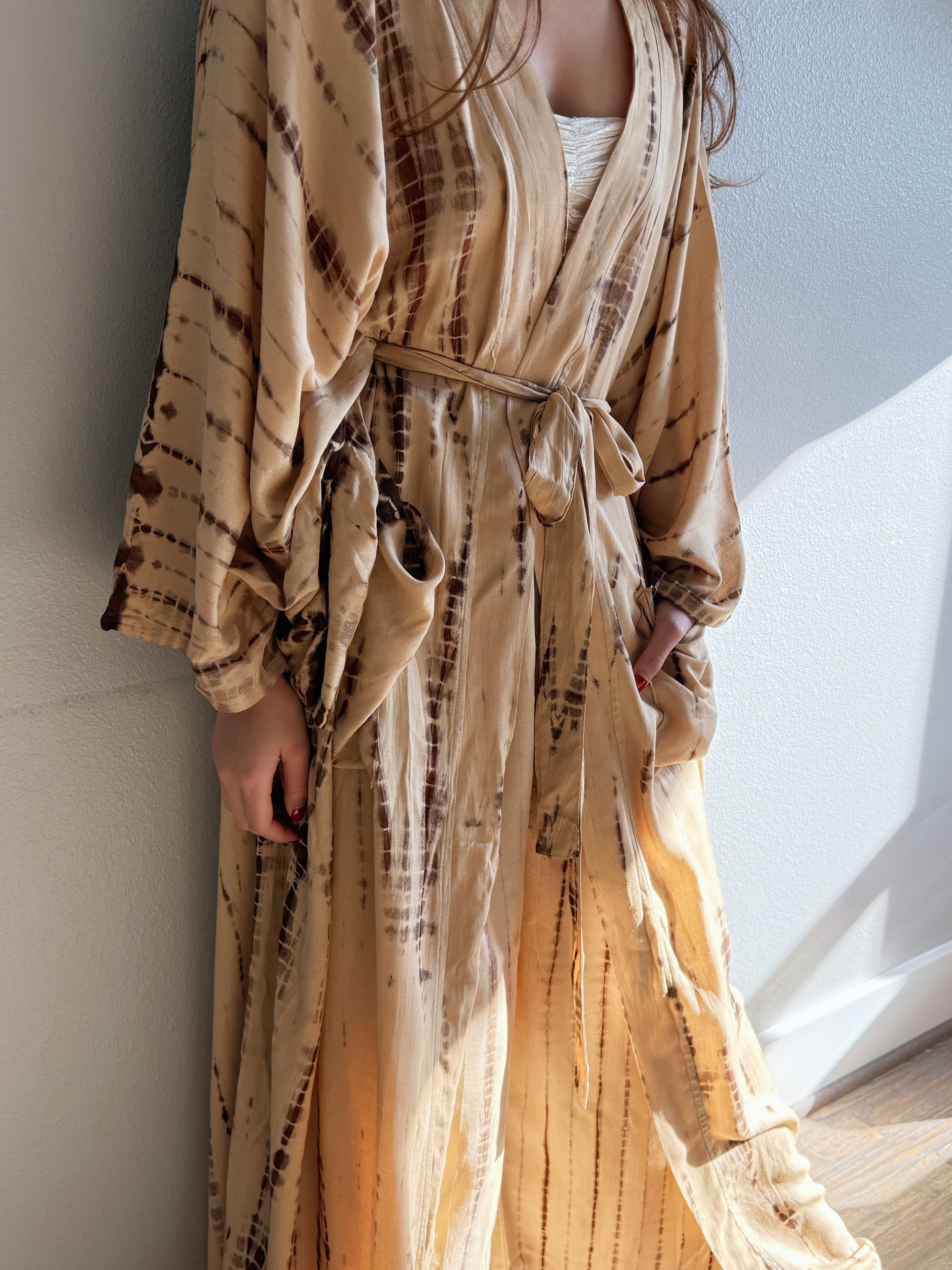 Woman wearing a tan tie-dye long kimono robe from Coco de Chom. The oversized robe features long sleeves, a waist tie, and a relaxed, boho-style fit.