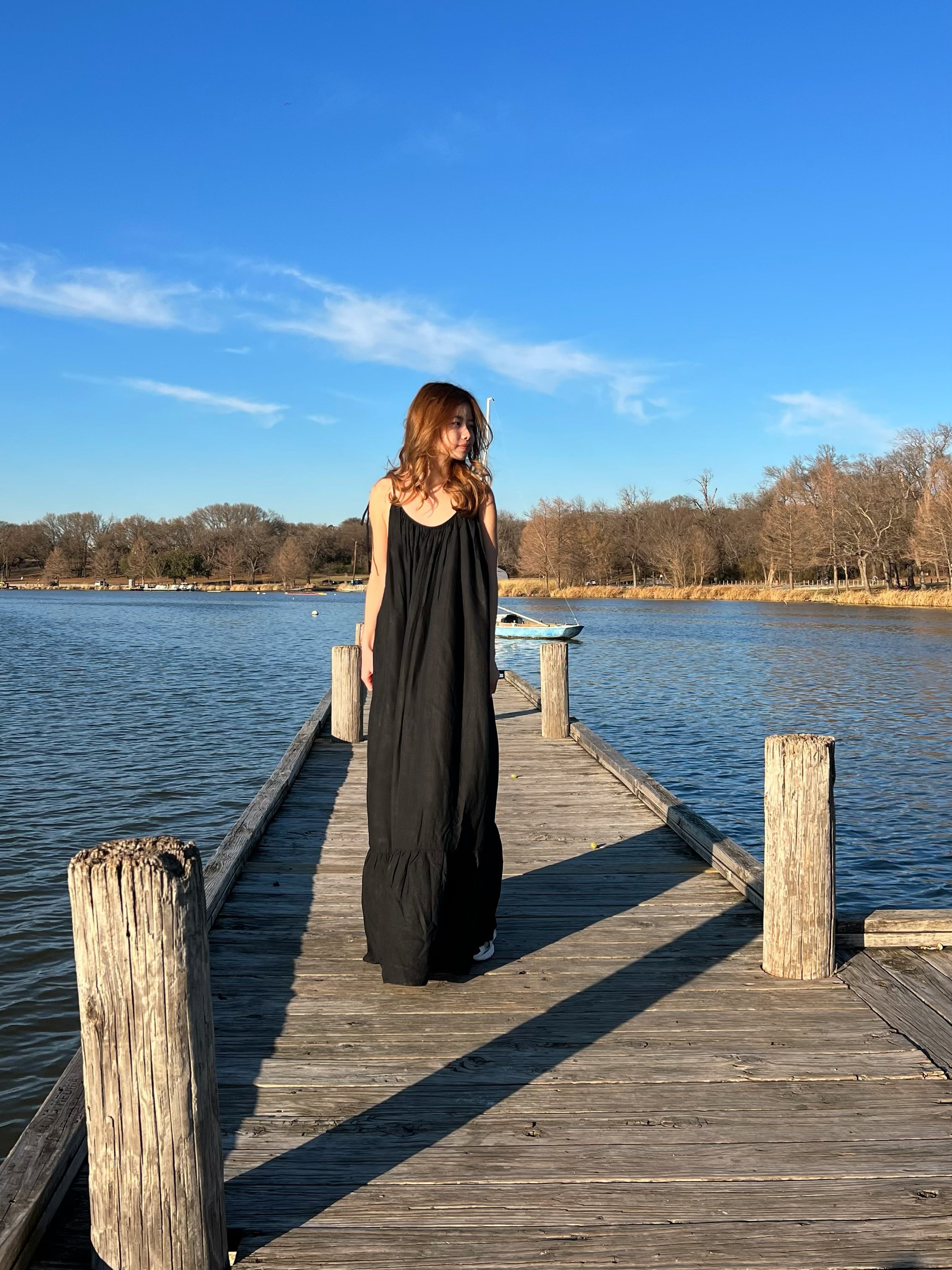 Woman in a hand-dyed black backless maxi dress standing by the sea, wearing boho resortwear by Coco de Chom