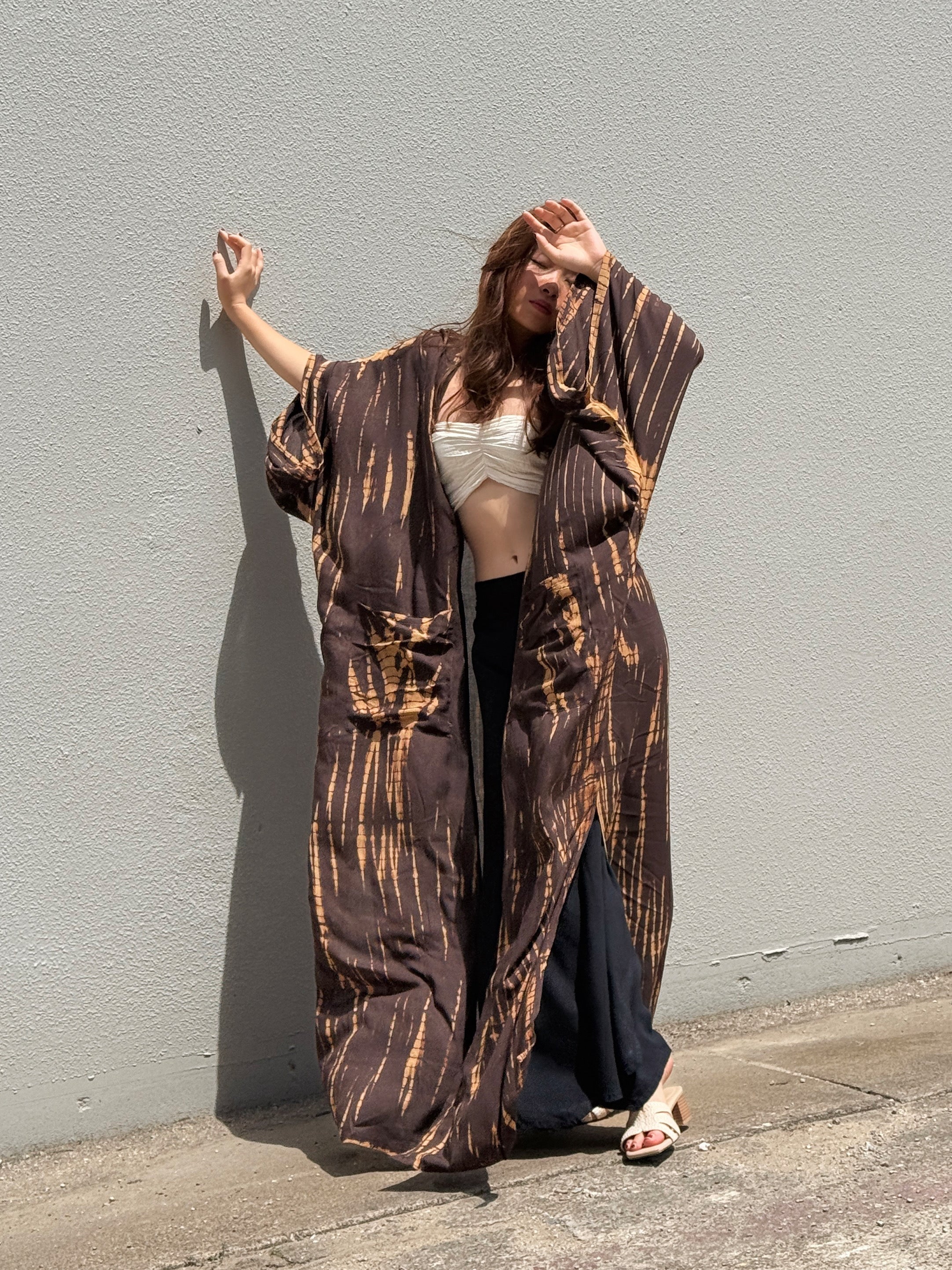Woman wearing a handmade long tie-dye kimono robe in brown with long sleeves and adjustable waist tie, styled as a boho duster and lightweight beach cover-up by Coco de Chom.