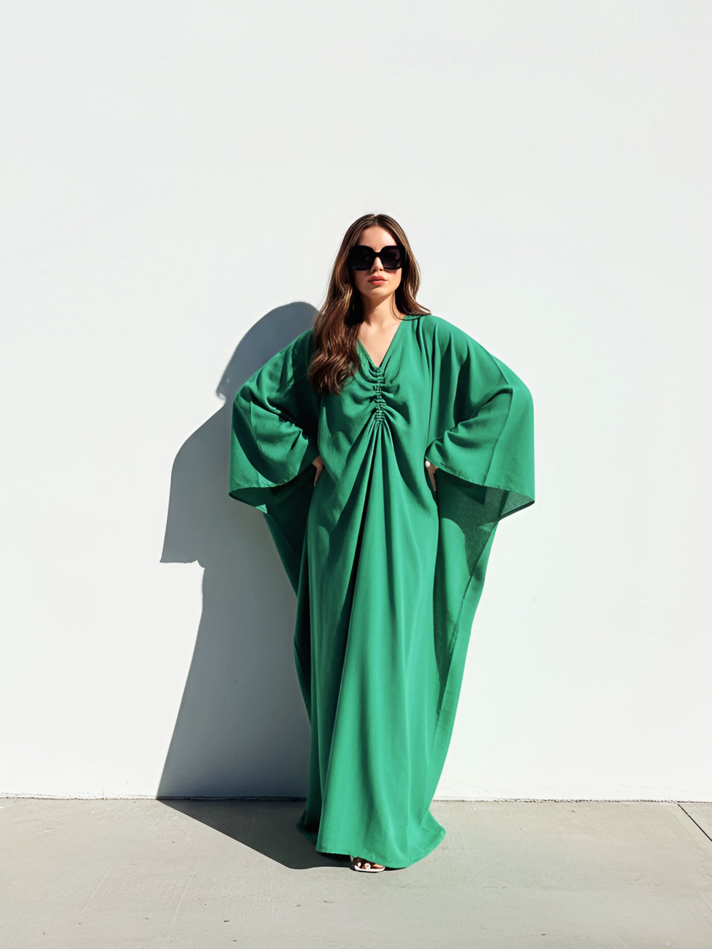 Woman wearing an Emerald green kaftan maxi dress by COCO DE CHOM, oversized plus size resort wear with long sleeves, flowy drape, and beach cover up maxi silhouette