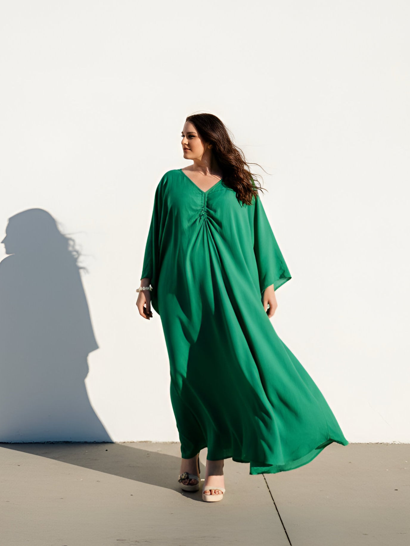 Woman wearing an Emerald green kaftan maxi dress by COCO DE CHOM, oversized plus size resort wear with long sleeves, flowy drape, and beach cover up maxi silhouette
