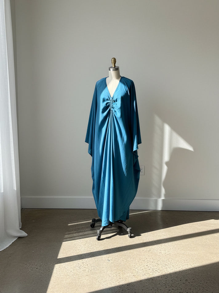 Teal Blue kaftan dress on a mannequin against a white wall with sunlight casting shadows.