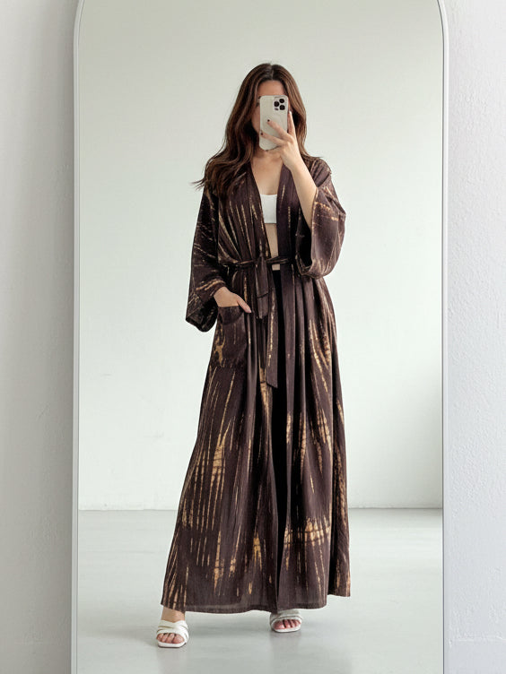 Woman lounging in oversized long tie dye kimono robe in brown, relaxed vacation boho look