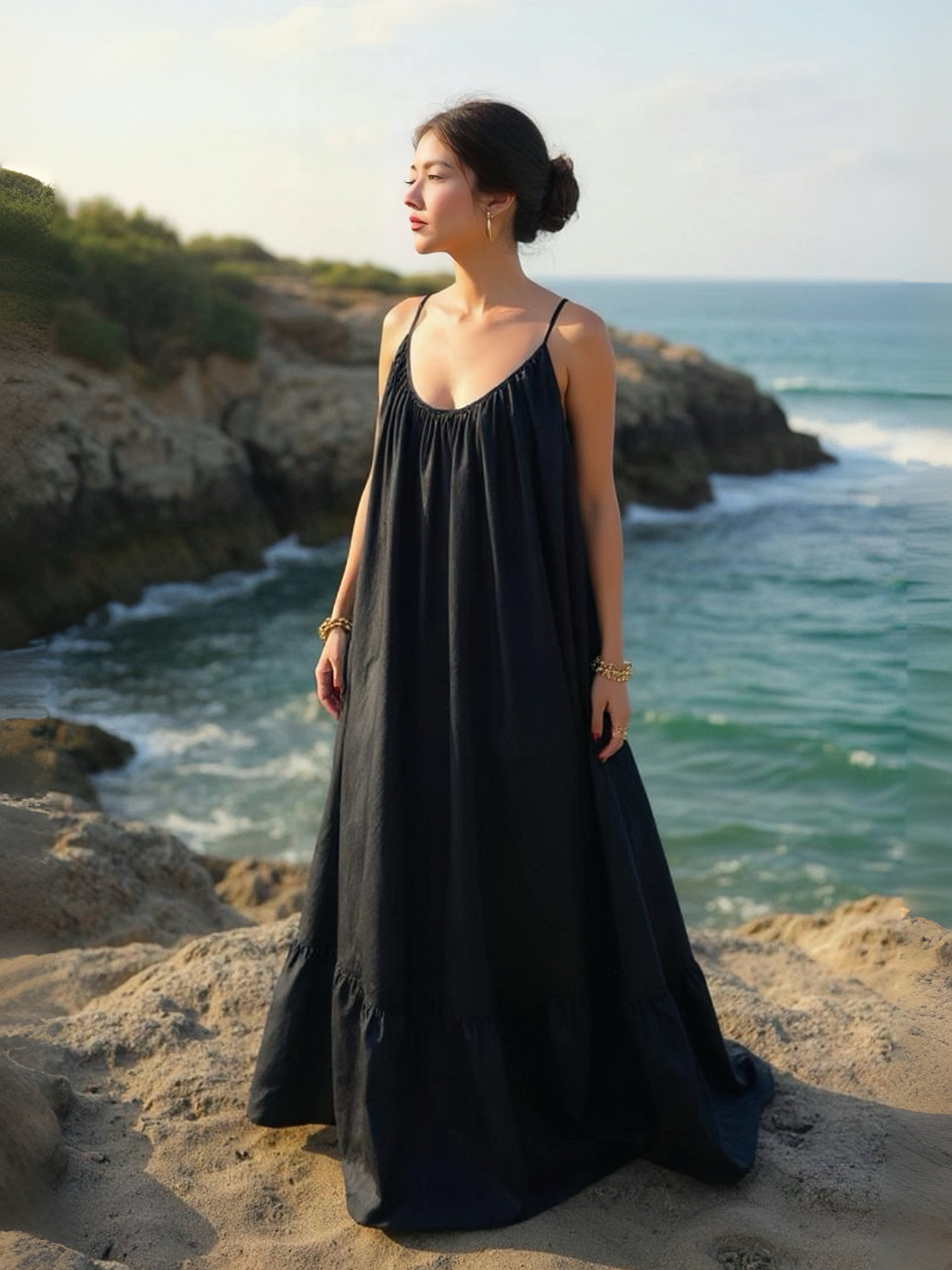 Woman in a hand-dyed black backless maxi dress standing by the sea, wearing boho resortwear by Coco de Chom