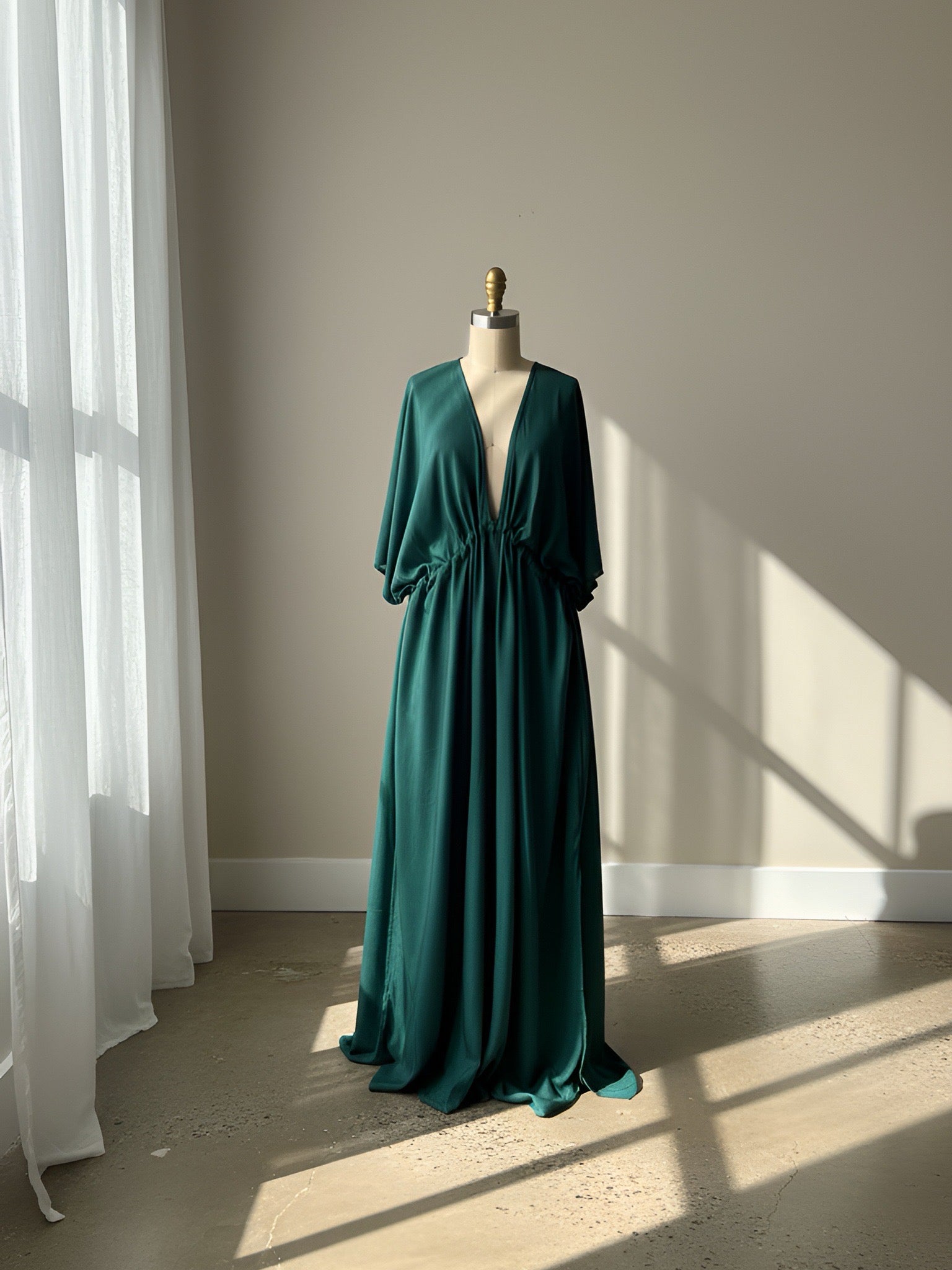 Green evening gown, klgreen kaftan dress on a mannequin against a neutral wall with sunlight casting shadows.