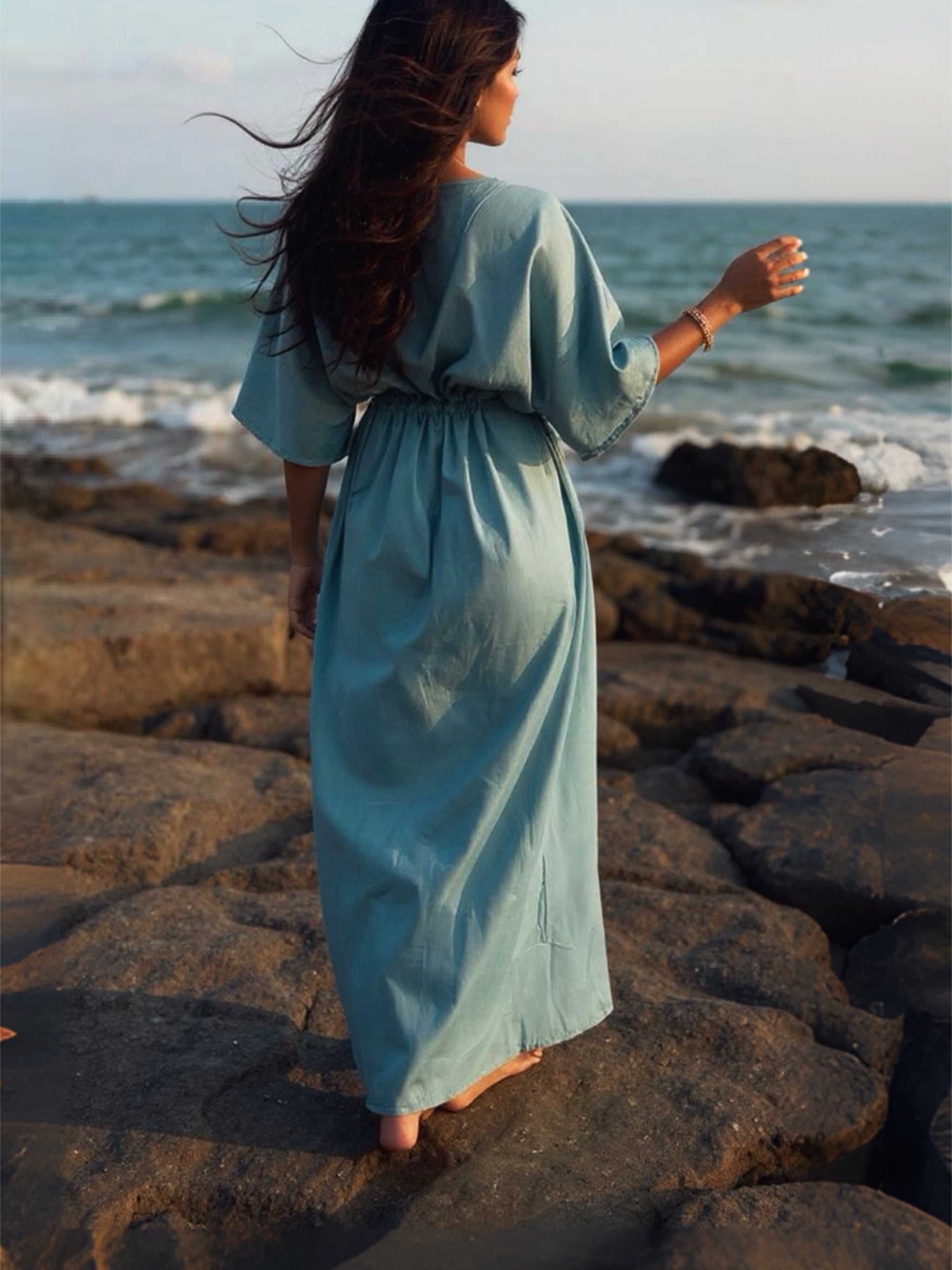 Woman wearing teal tie dye goddess kaftan maxi dress with sunglasses and straw hat on a tropical beach