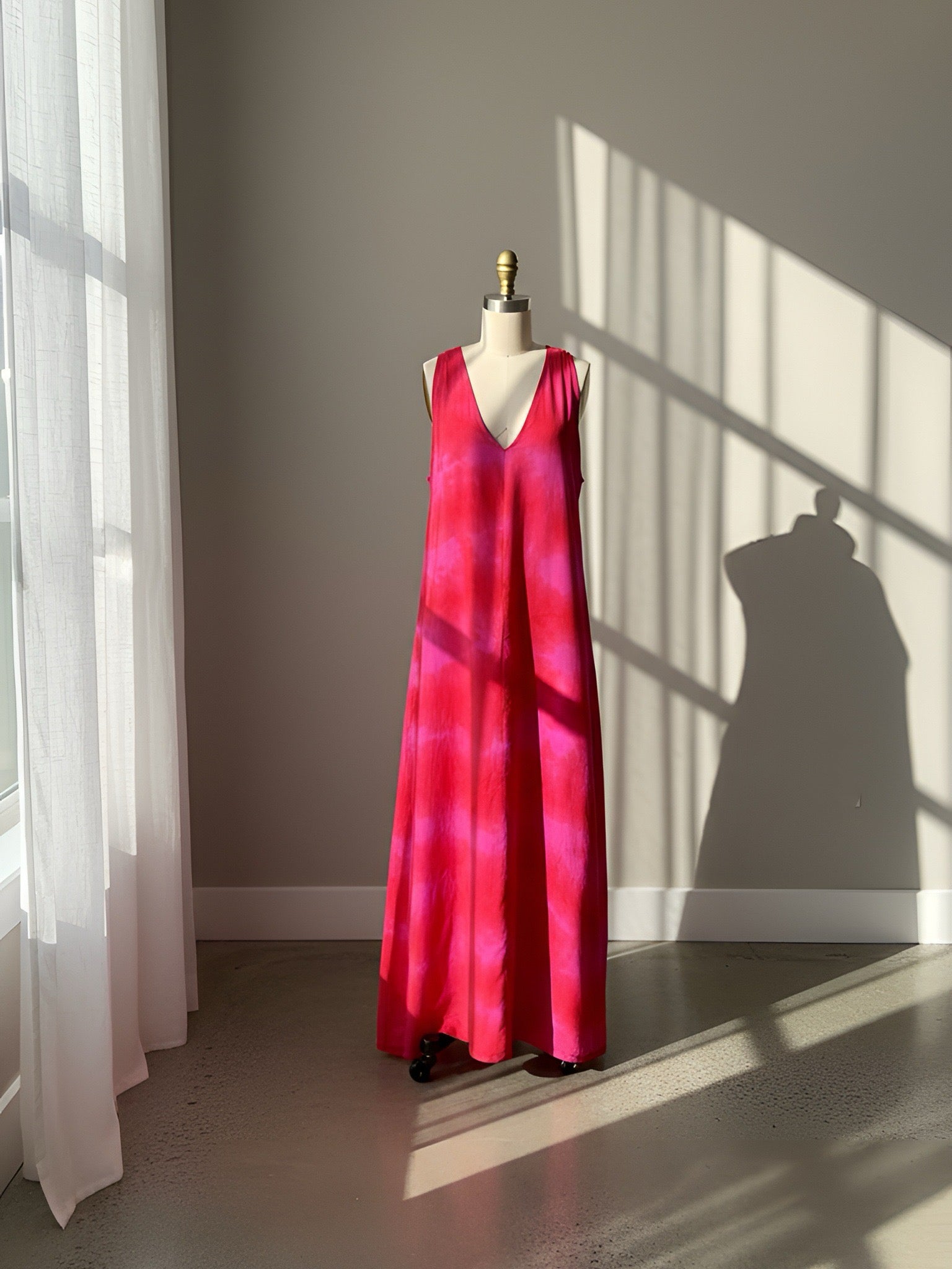 Red and pink tie-dye maxi dress on a mannequin against a neutral wall with sunlight casting shadows.