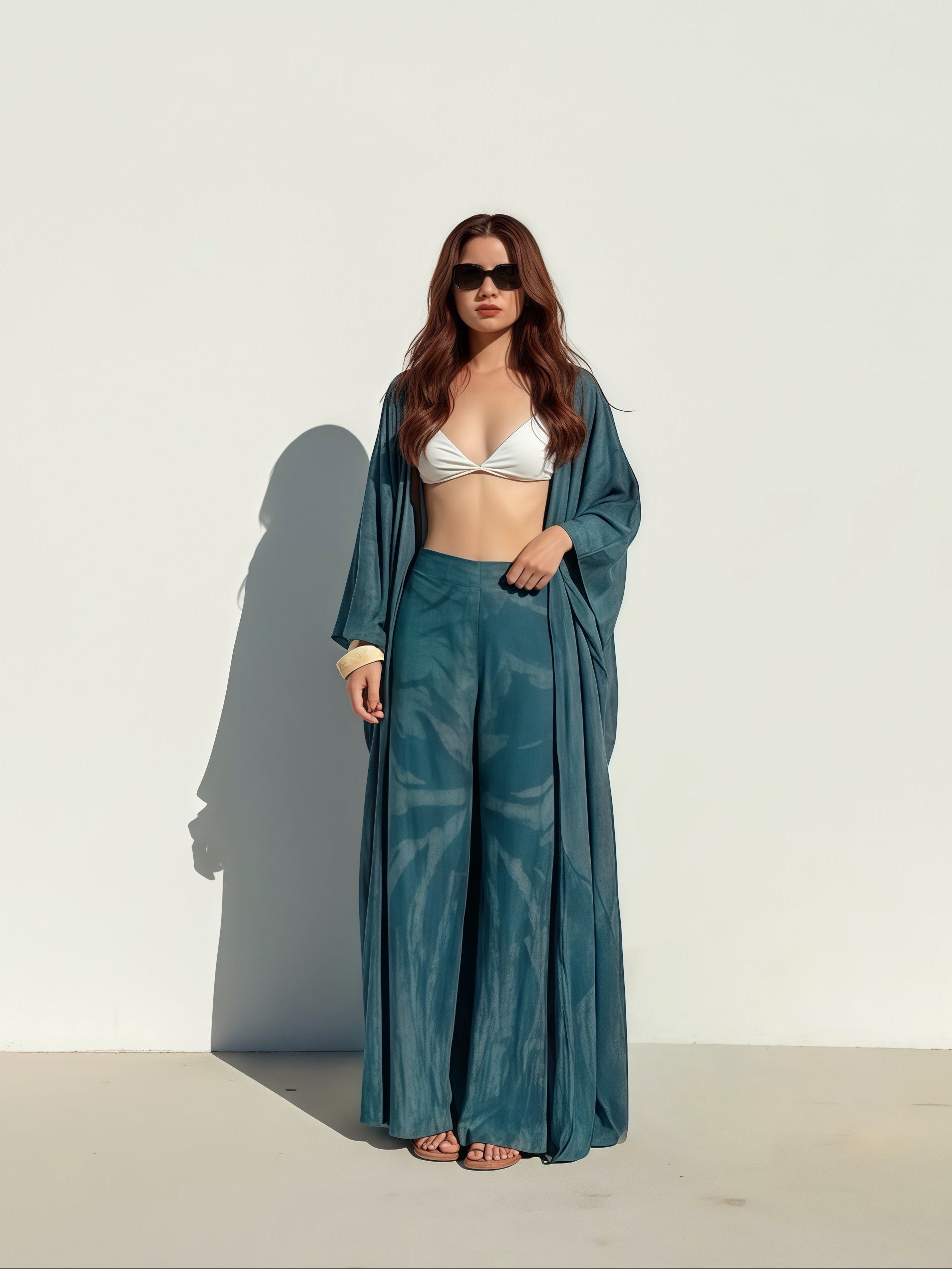 Woman wearing a white bikini top and teal tie dye kimono-style garment against a white background during her vacation