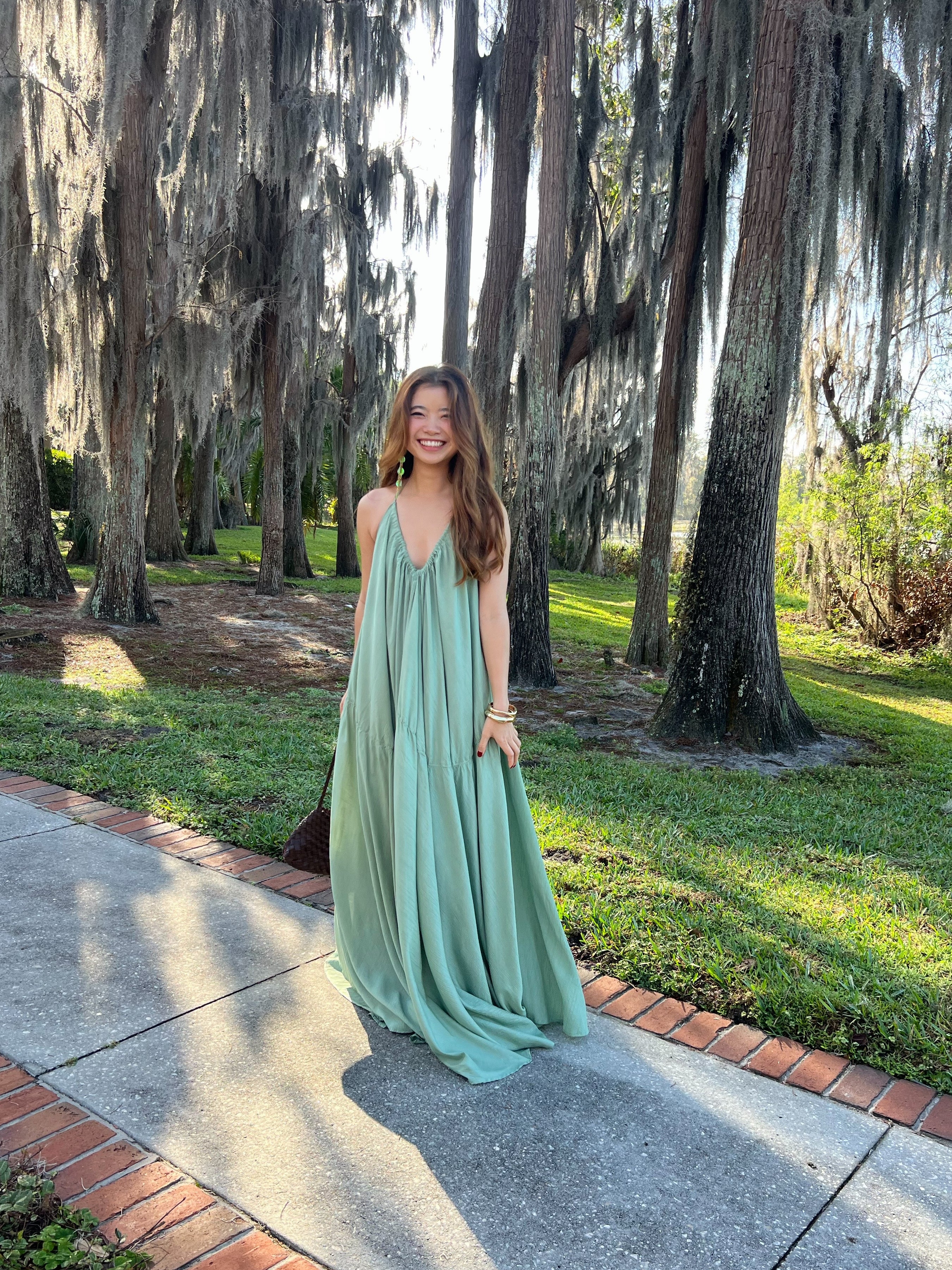 Woman in a green dress standing in a park with trees and grass.