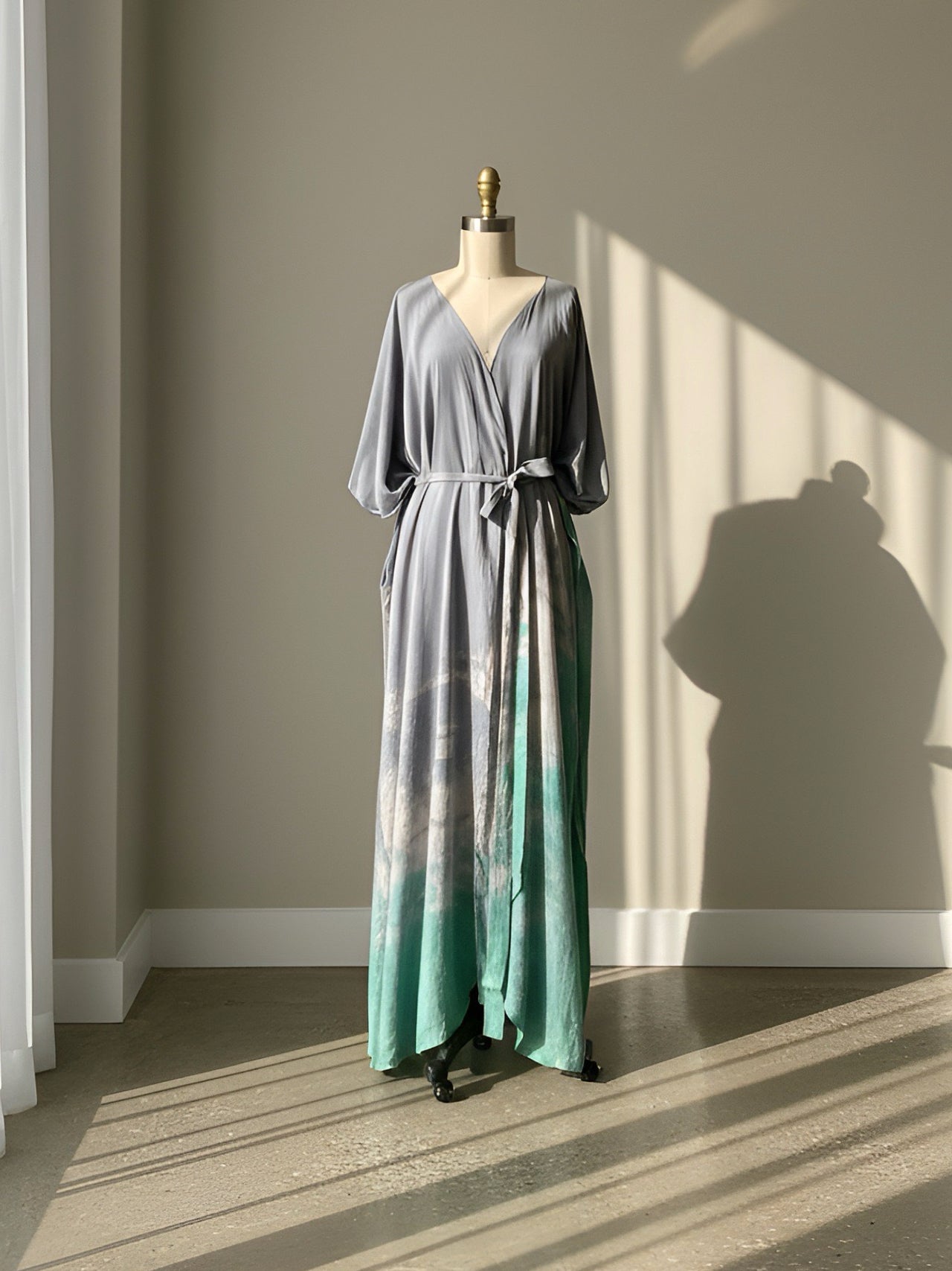 Tie dye kimono robe dress on a mannequin against a neutral wall with sunlight casting shadows.