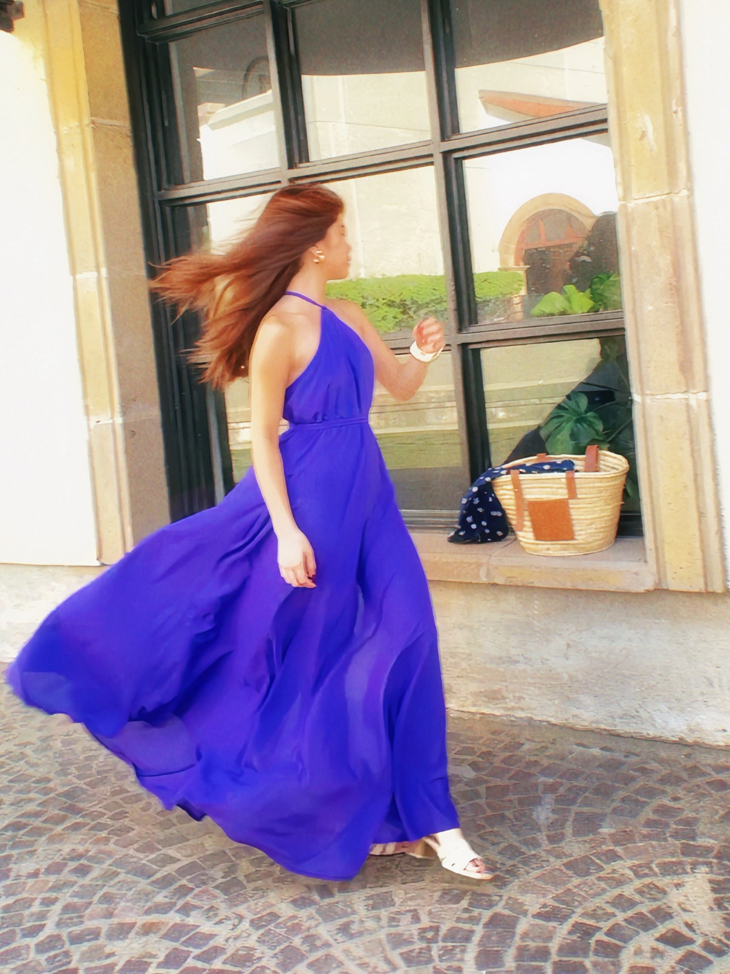 Woman in a dyed vivid bold blue halter maxi dress standing in front of a building entrance.