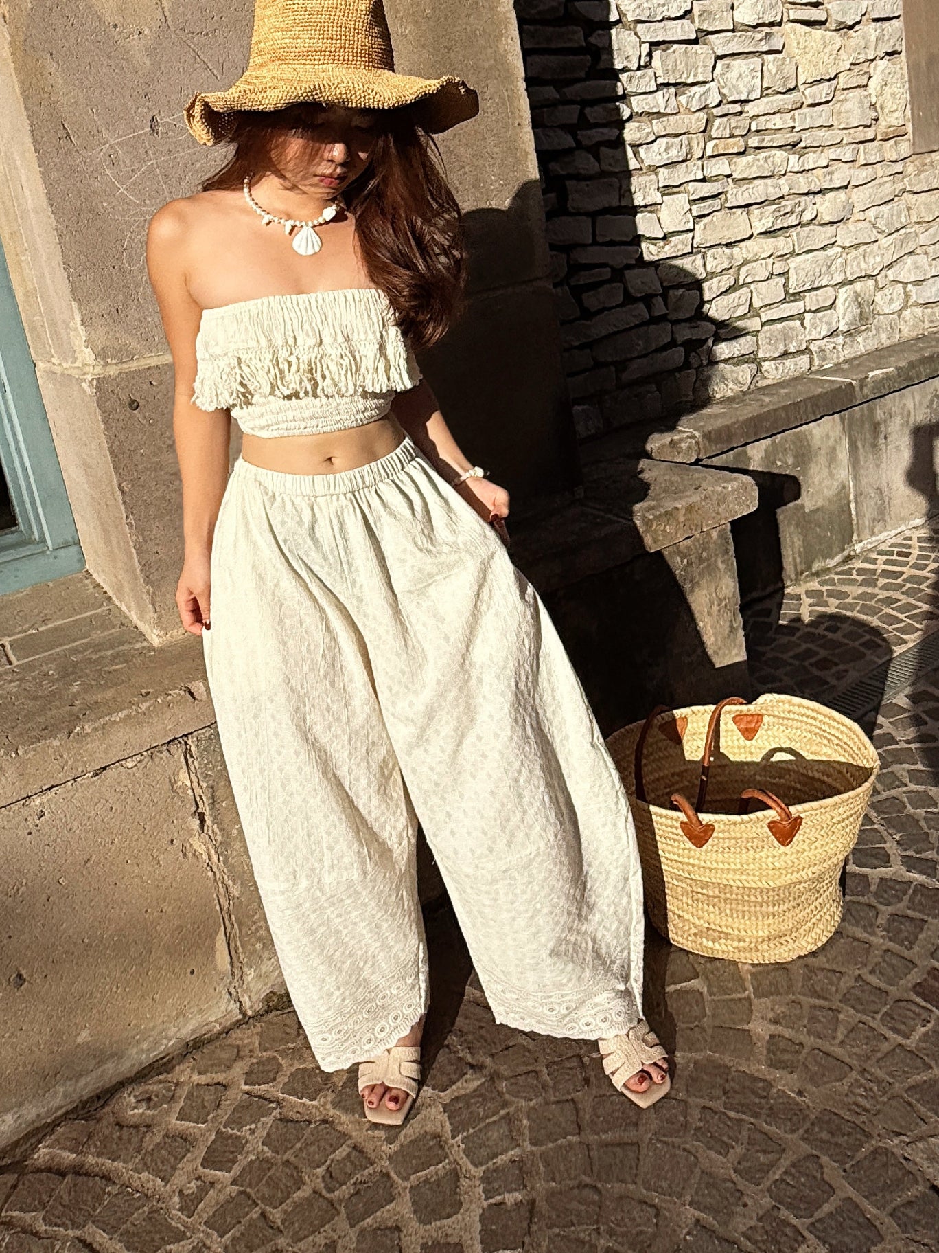 Woman wearing ivory wide leg cotton pants with lace hem, styled barefoot with straw tote — boho beach outfit for summer, handmade resortwear