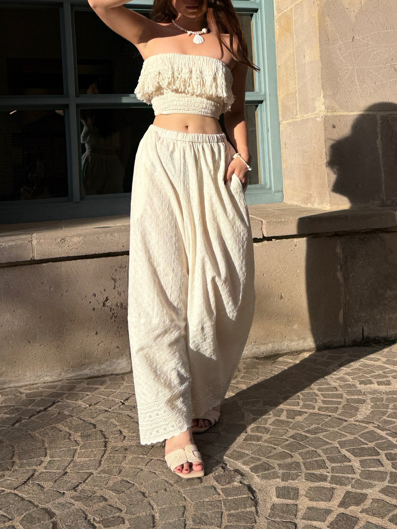 Woman wearing ivory wide leg cotton pants with lace hem, styled barefoot with straw tote — boho beach outfit for summer, handmade resortwear