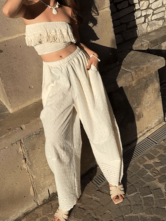 Woman wearing ivory wide leg cotton pants with lace hem, styled barefoot with straw tote — boho beach outfit for summer, handmade resortwear