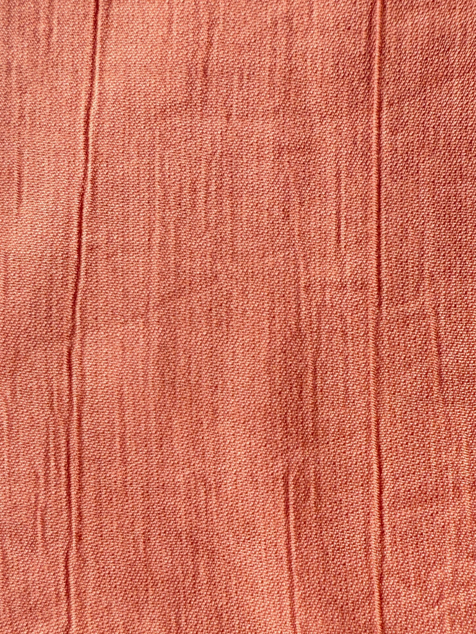 Close-up of a textured coral fabric with visible stitching lines.