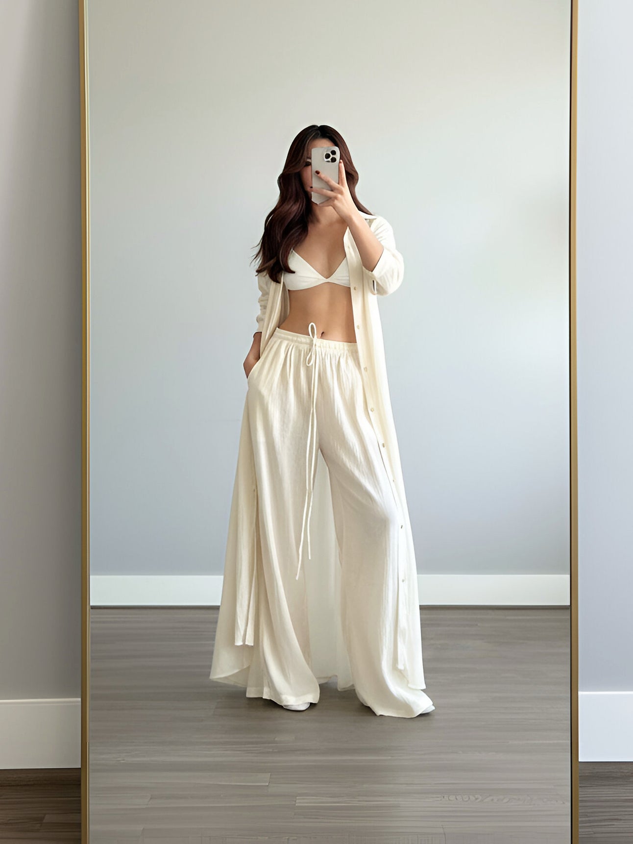 Woman taking a mirror selfie wearing an organic cotton pants, white outfit in a minimalistic room.