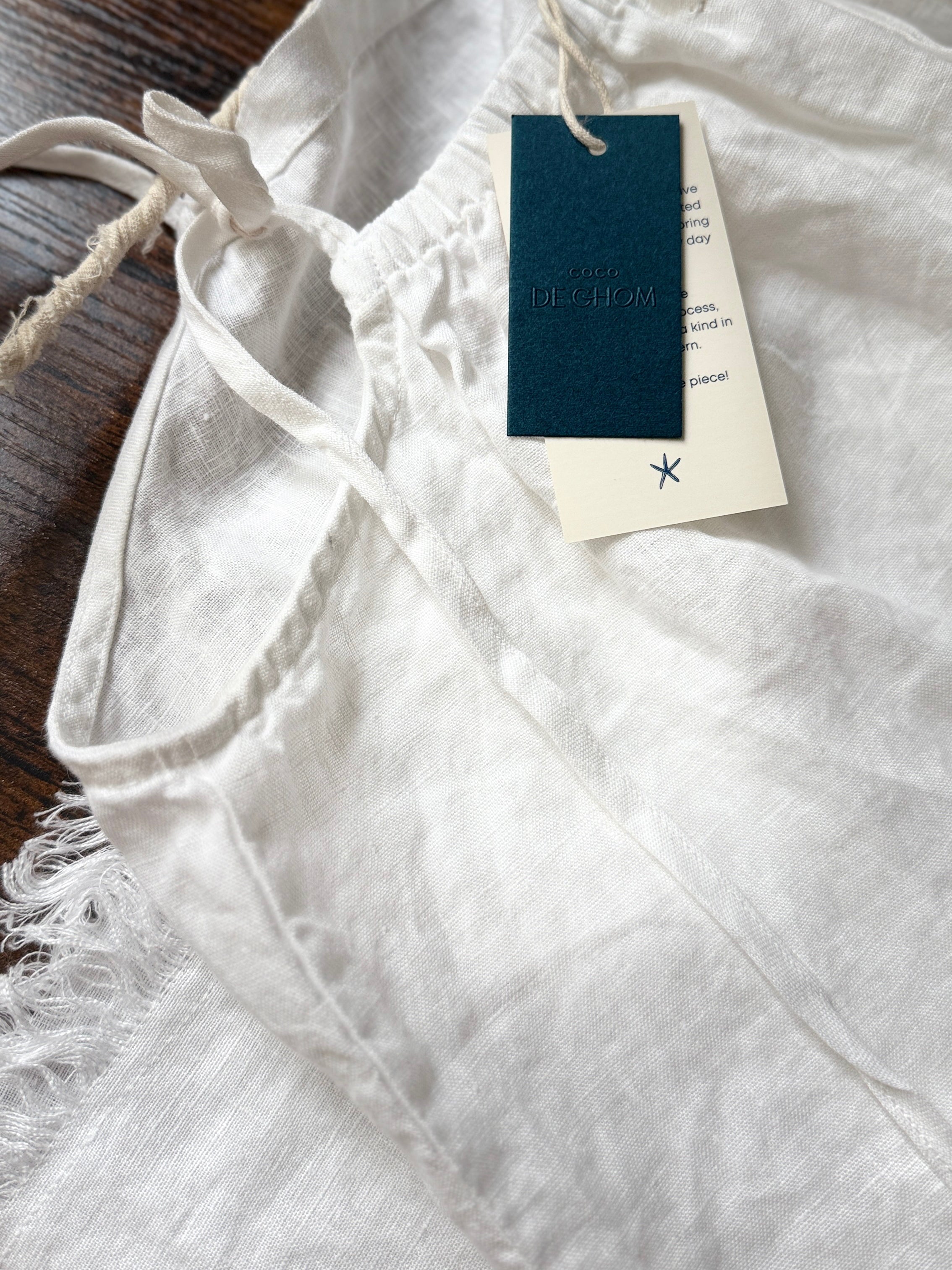 Flat lay of white linen dress on neutral background – eco-friendly summer wardrobe essential