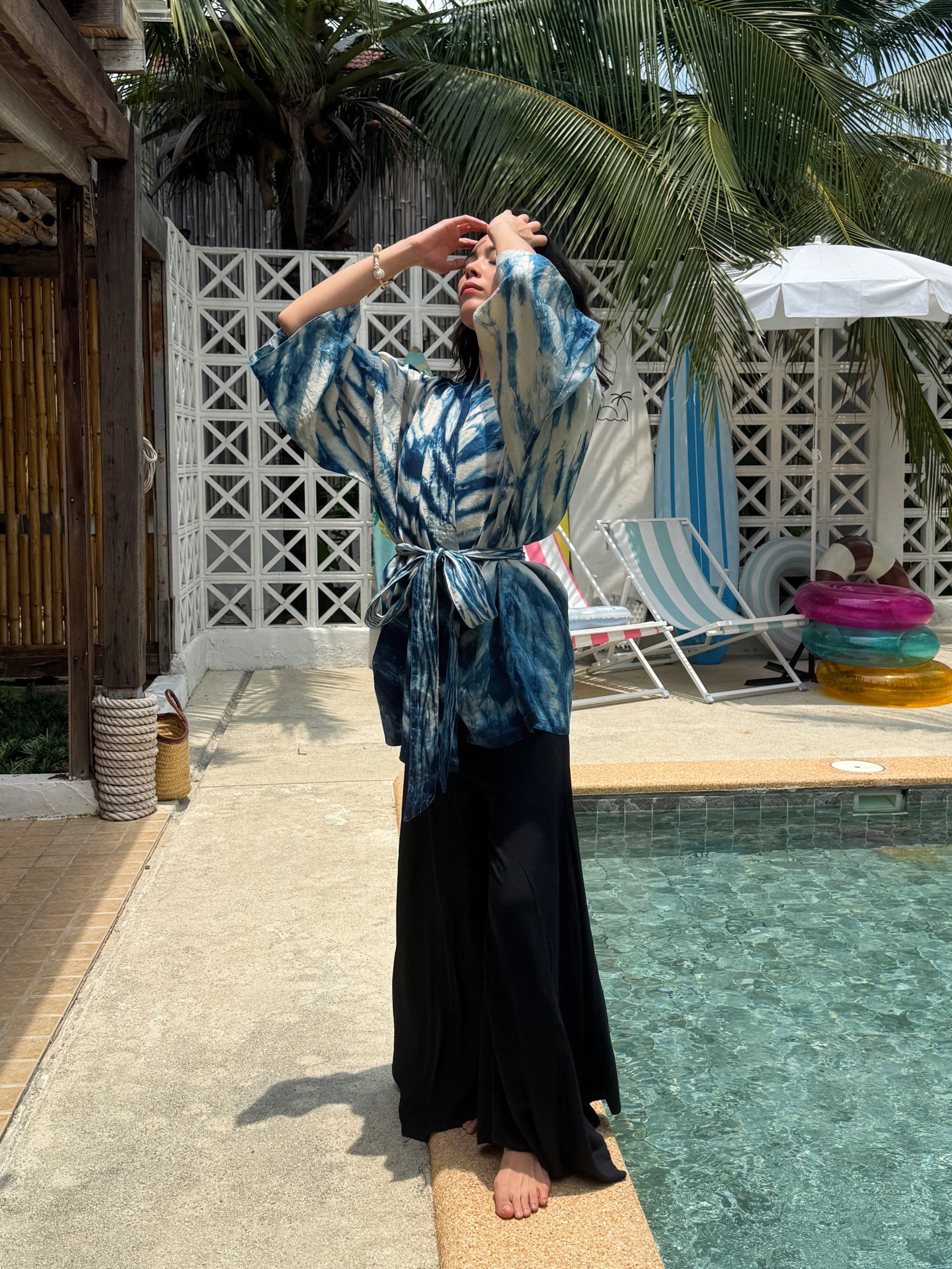Model wearing the Limited Edition Kira Indigo Linen Kimono, artisan handmade with natural indigo Shibori tie dye. Features wide sleeves, a linen belt, and a relaxed Japanese kimono wrap silhouette. Perfect for sustainable fashion lovers seeking a boho kimono jacket or limited edition slow fashion robe from COCO DE CHOM.