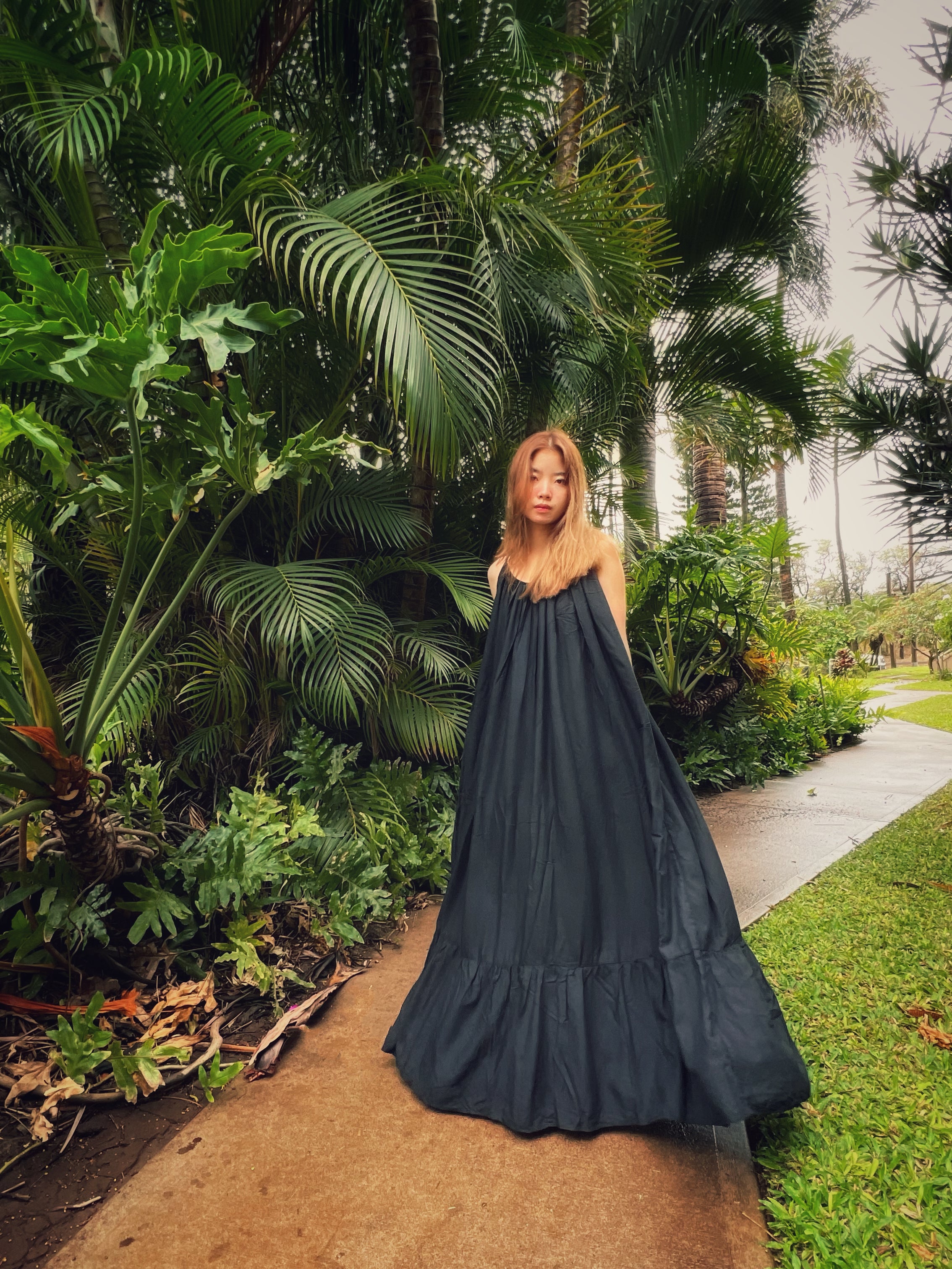 Woman in a hand-dyed black backless maxi dress standing by the trees, wearing boho resortwear by Coco de Chom