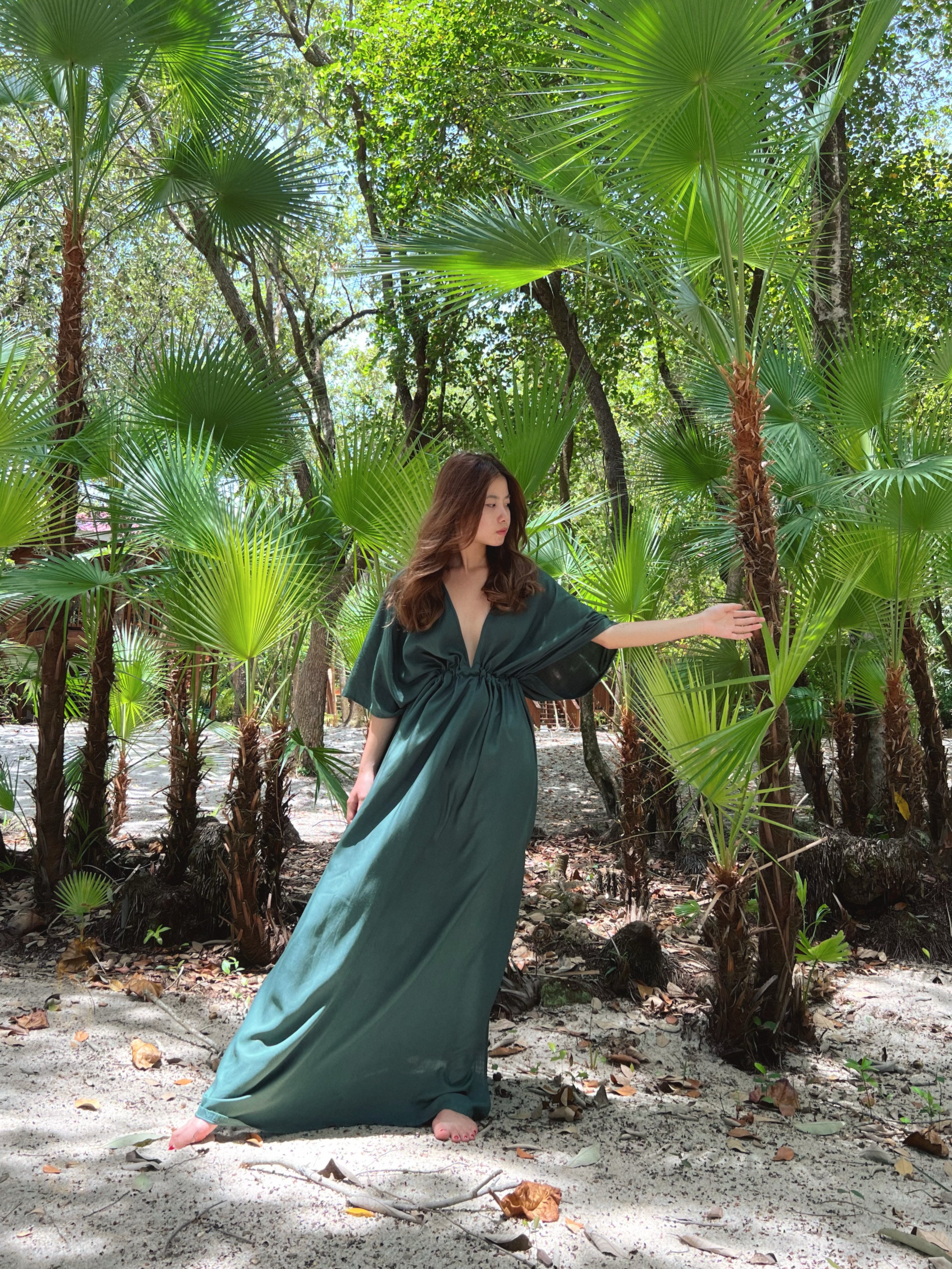 Woman wearing a flowy tie-dye kaftan maxi dress on the beach, featuring a deep V-neck, side slit, and cinched waist—handmade resortwear by Coco de Chom