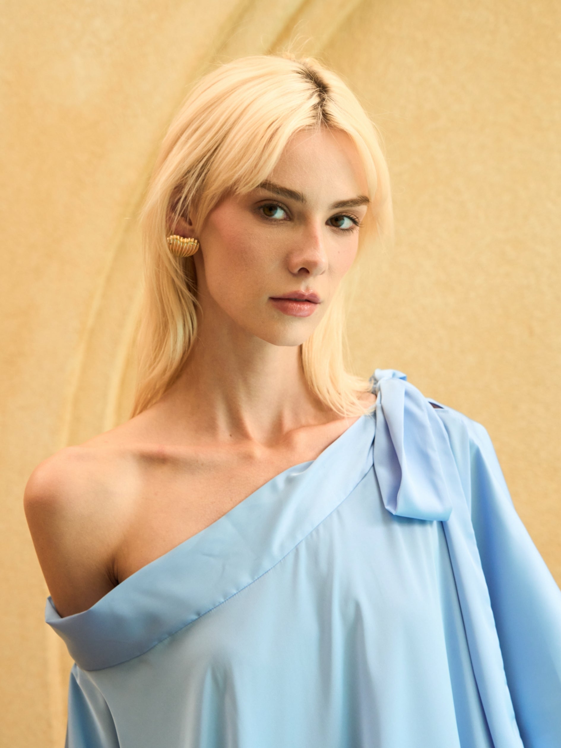 Woman wearing a light blue one-shoulder dress against a beige background