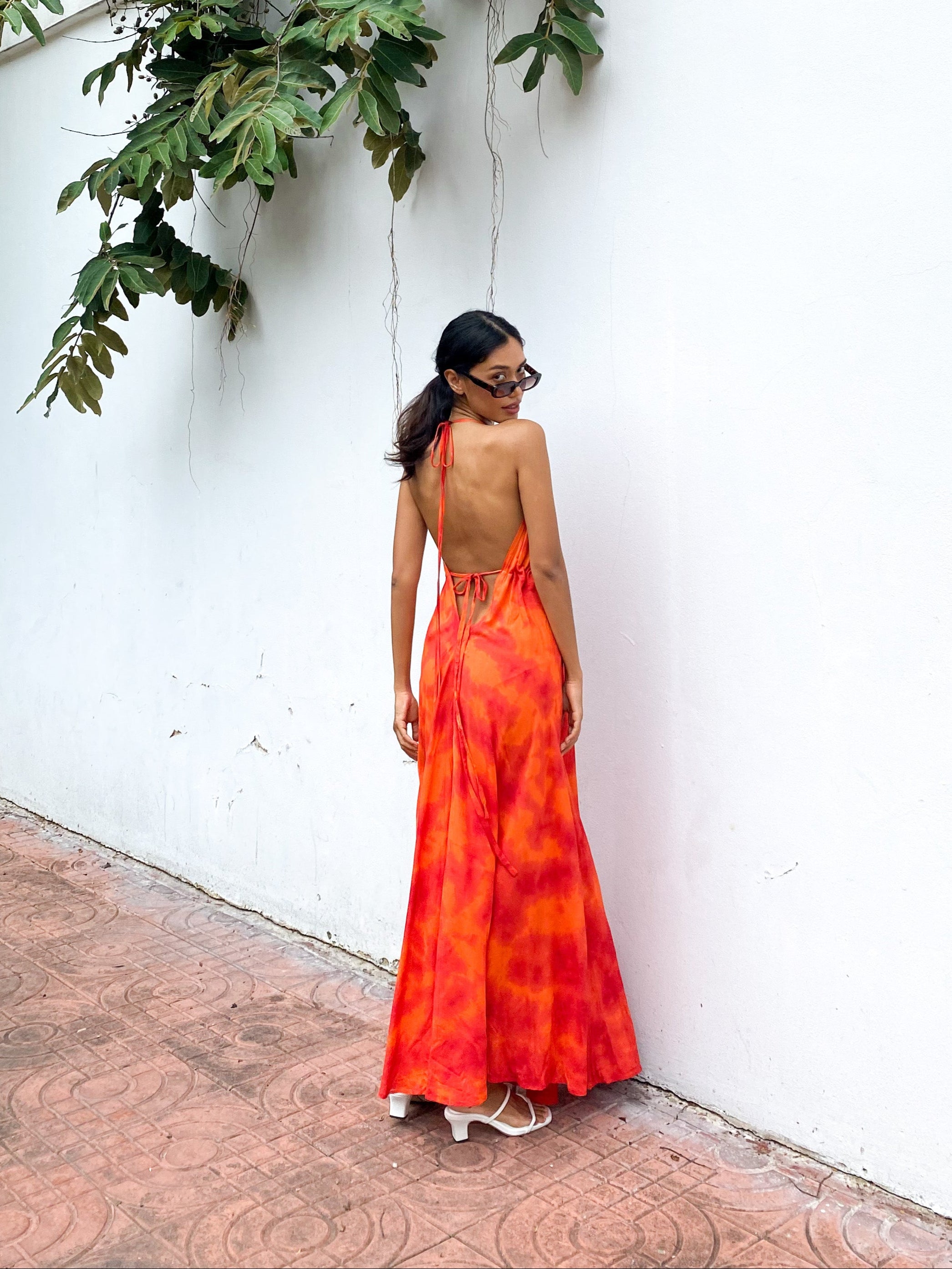 Woman wearing an orange tie-dye open Back Halter Maxi Dress in vibrant orange tie-dye, featuring a flowing maxi length and backless halter design—perfect vacation dress by Coco De Chom.