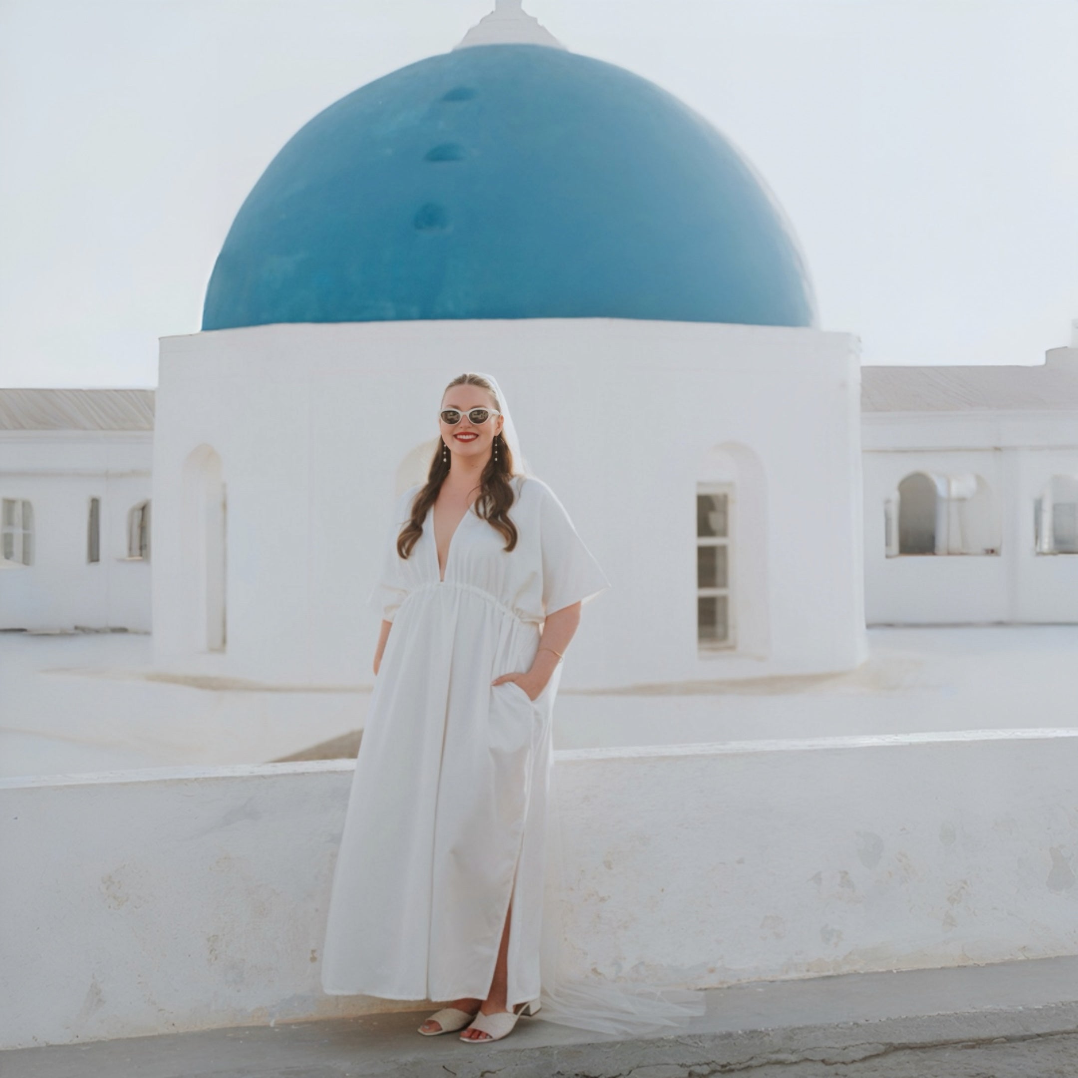 Bride in a custom white COCO DE CHOM kaftan wedding dress on a rooftop overlooking a blue-domed church in Santorini
