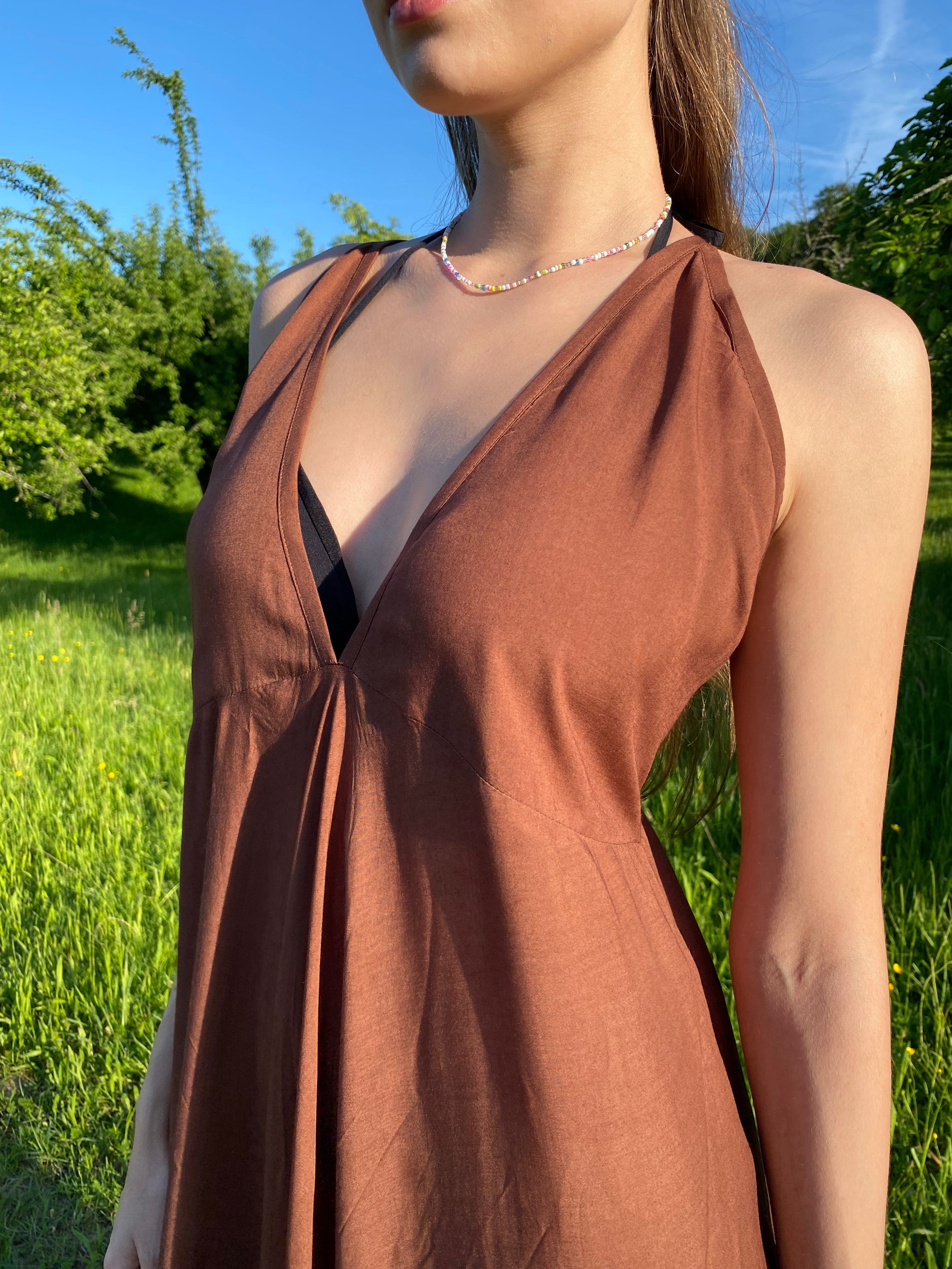 Close up front view of a woman in a toffee brown halter maxi dress deep v neckline with long wrap ties, open back, and flowy silhouette, perfect for summer vacations.