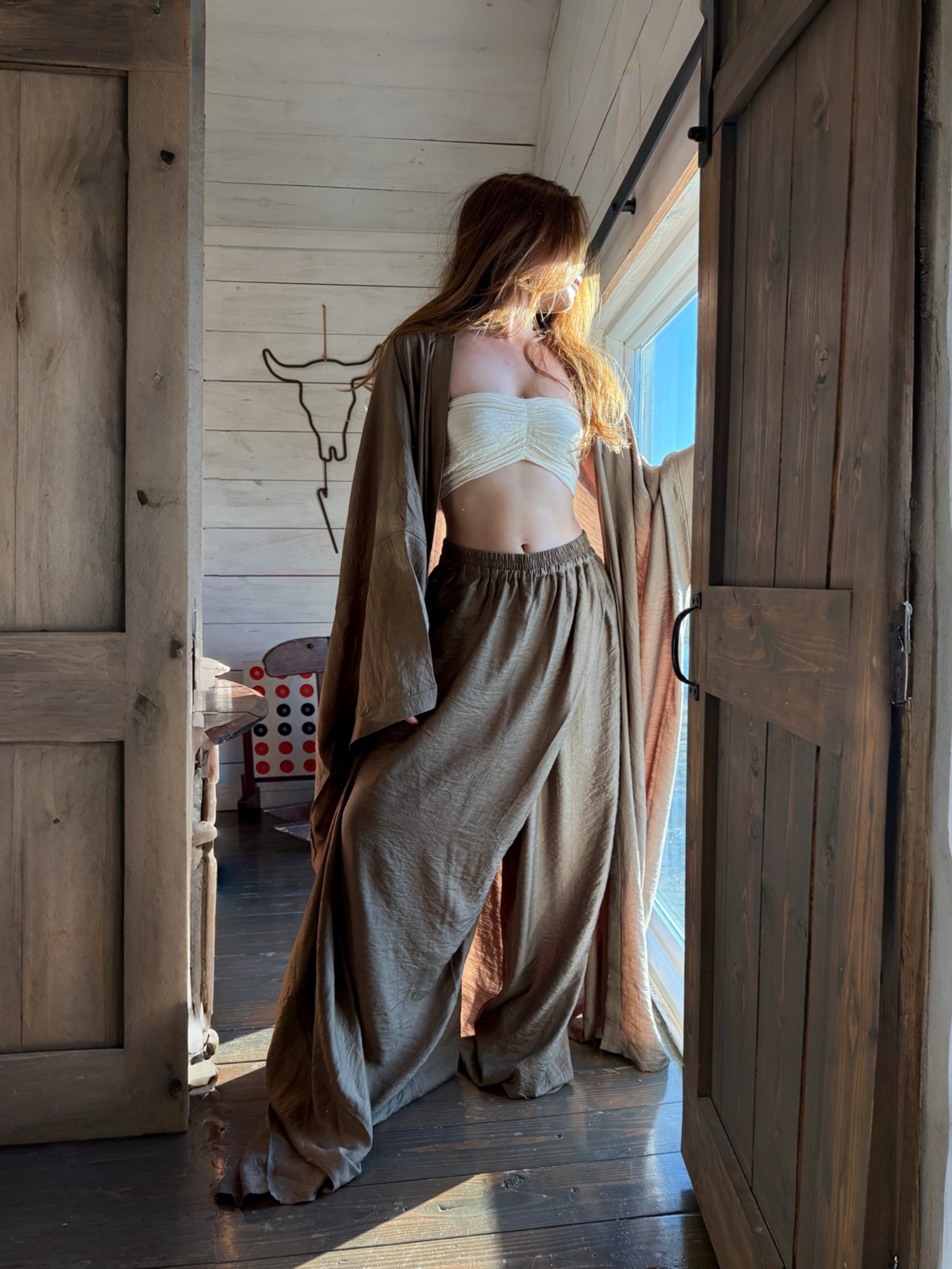 Woman in a flowing outfit standing in a doorway with wooden doors and a bright light source.