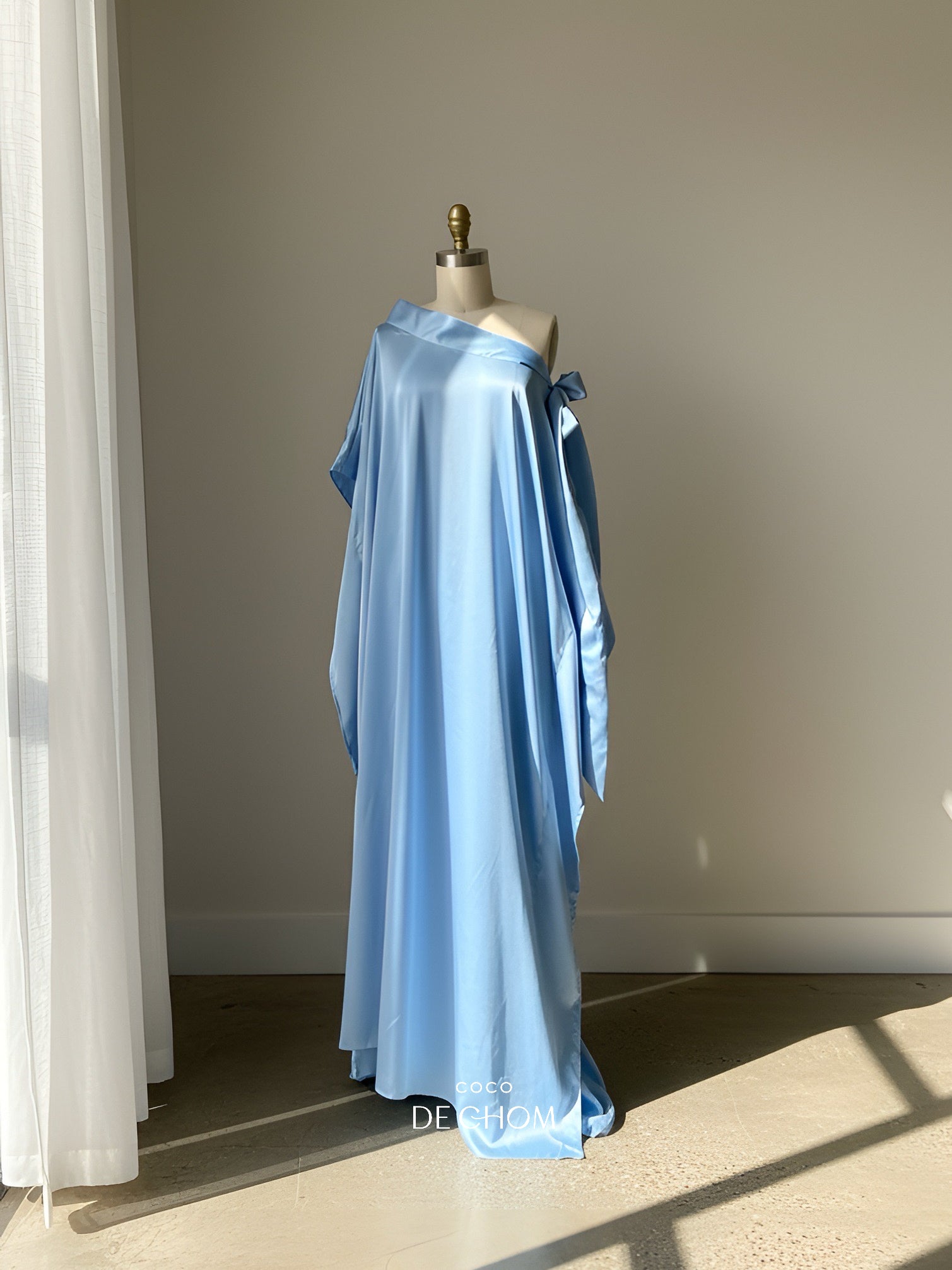 Woman wearing a sky blue off shoulder kaftan maxi dress with a flowy silhouette, styled as a beach wedding guest dress and resort wear by COCO DE CHOM