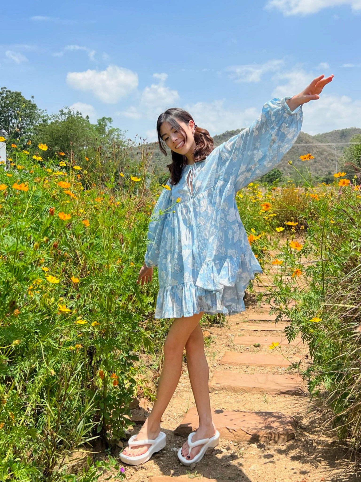 Discover Coco de Chom the Lola Bohemian Mini Dress in Beautiful Blue Sky: A Truly Unique Limited Edition Piece. Lola's Captivating Design is Handcrafted Using Wooden Blocks on Fine Cotton Voile, Featuring a Dreamy Block Printed Pattern Inspired by Bougainvillea Flowers and Vacations. Perfect for Beach Days, Vacations, and Boho Lovers.