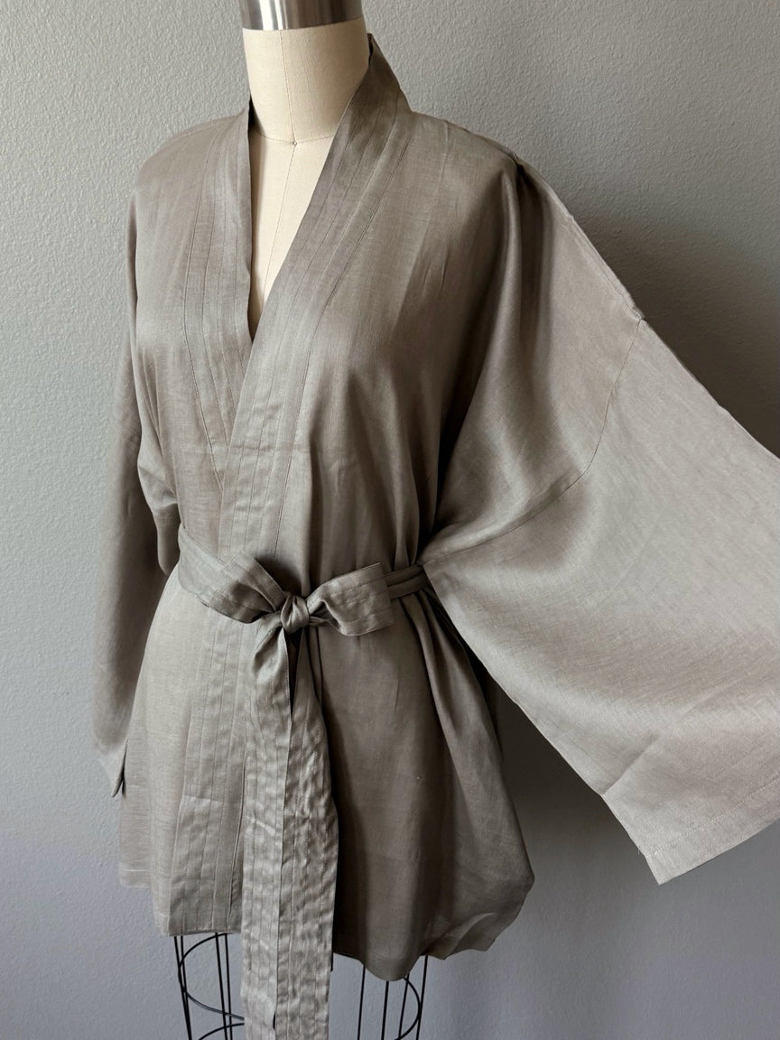 Natural gray linen kimono jacket with oversized wrap fit, wide sleeves, pockets, and removable waist tie, styled as a resort robe and everyday linen layer.
