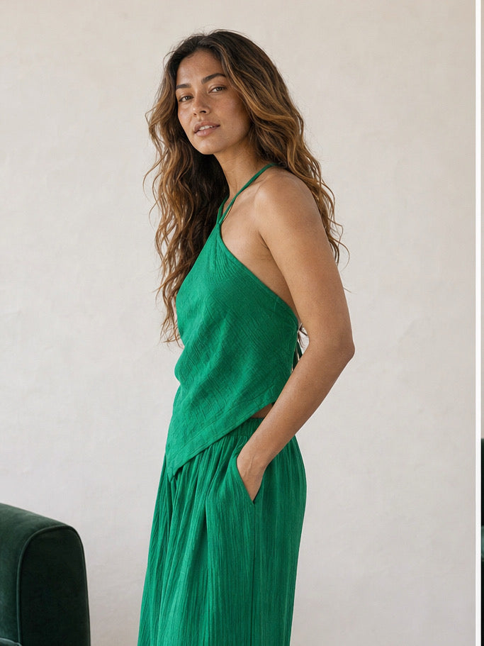 Woman wearing an emerald green handkerchief halter top and matching wide leg pants, boho vacation outfit and resort wear set for beach travel