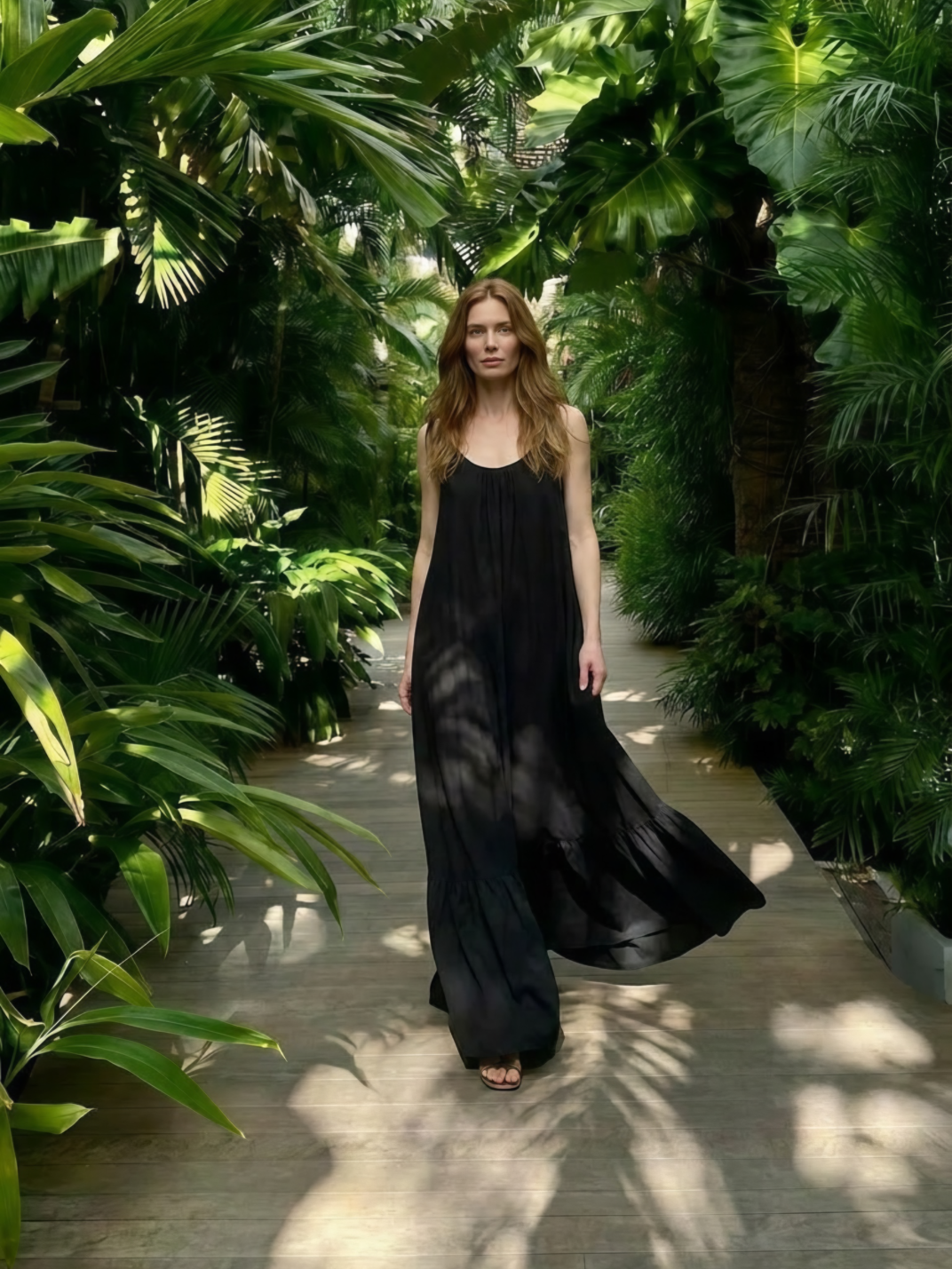Woman in a hand dyed black open back maxi dress walking through a lush green garden, look resort style perfect resort wear