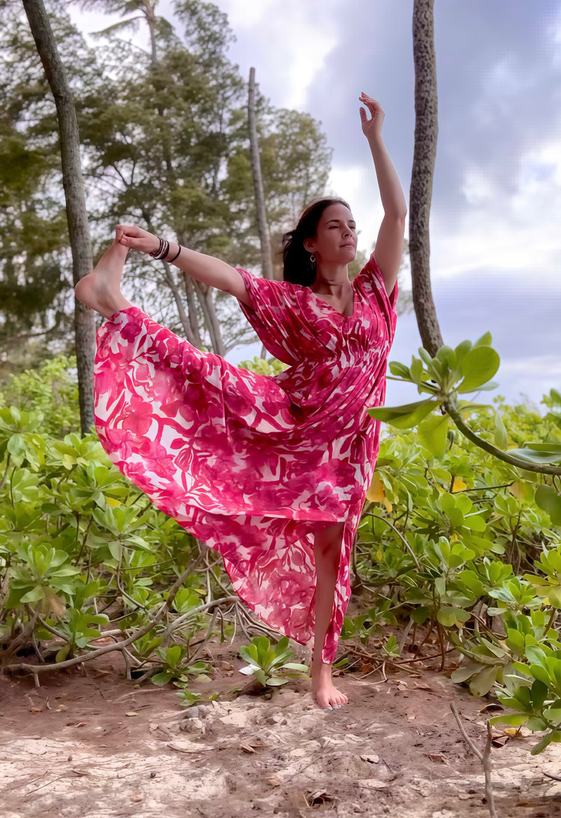 Woman in a pink floral kaftan dress standing on one leg in a forest setting