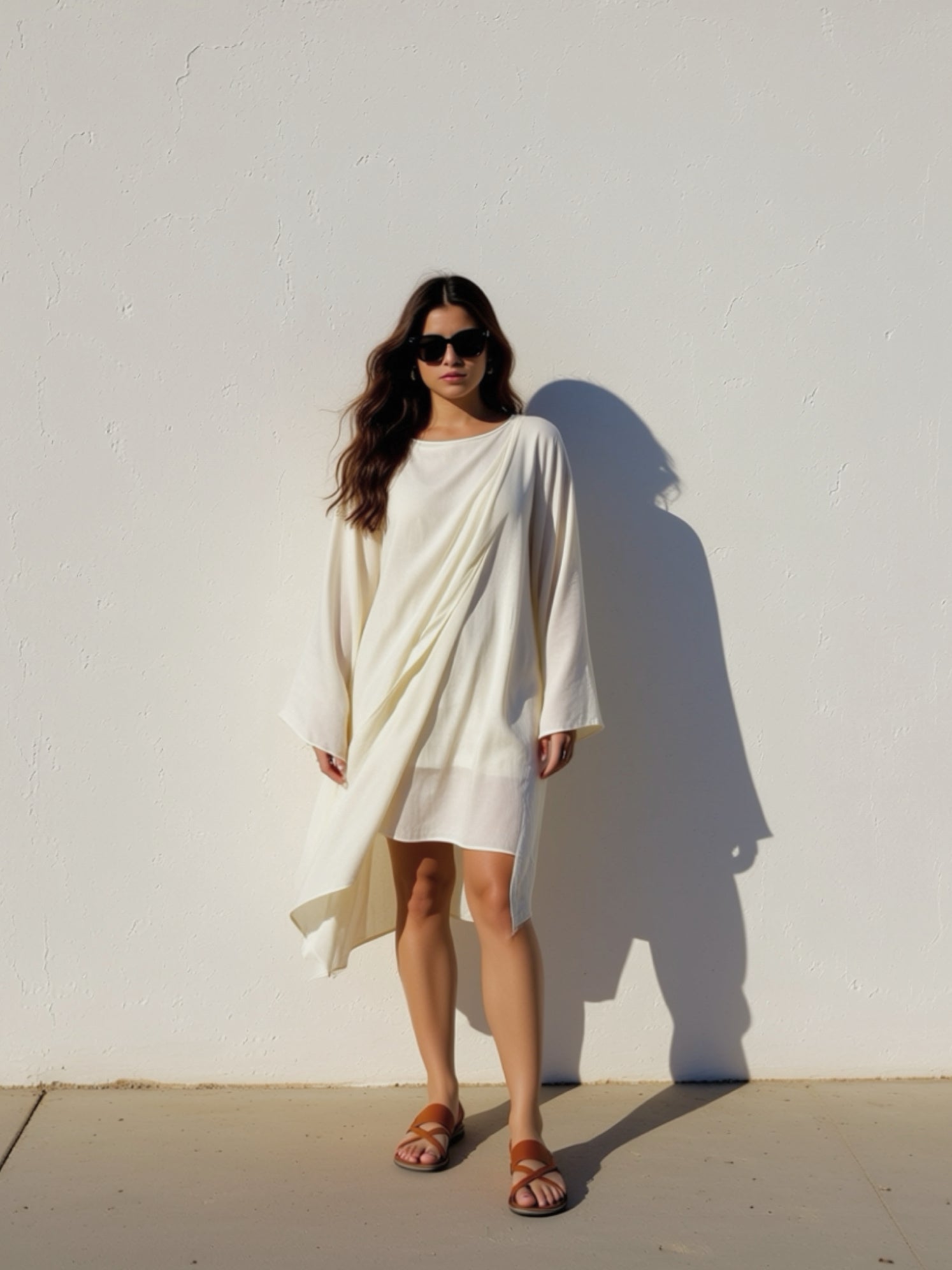 Woman wearing a white mini kaftan top beach cover up tunic, one size fits most, long sleeves with high-low hem, lightweight resort vacation wear, standing outdoor beach day.