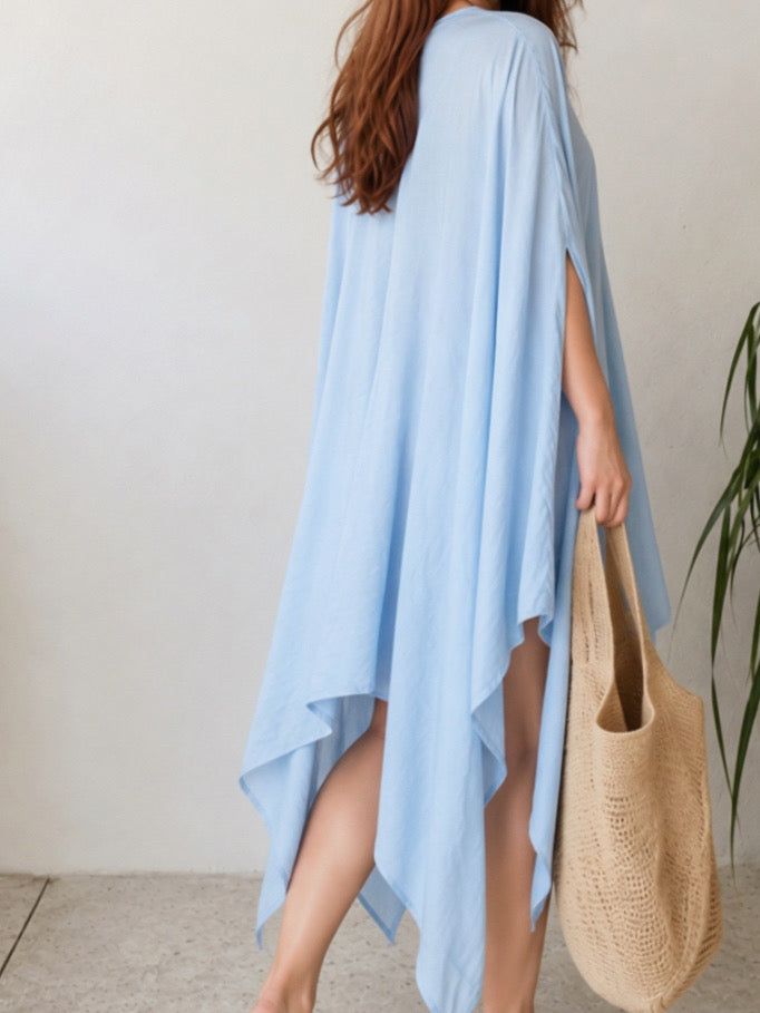 A woman modeling a light blue kaftan dress with a V-neckline and wide draped sleeves, standing against a neutral light gray background. Sky blue Soleil Mini Kaftan Cover Up, lightweight mini kaftan dress and beach cover up styled as a resort top for summer vacation