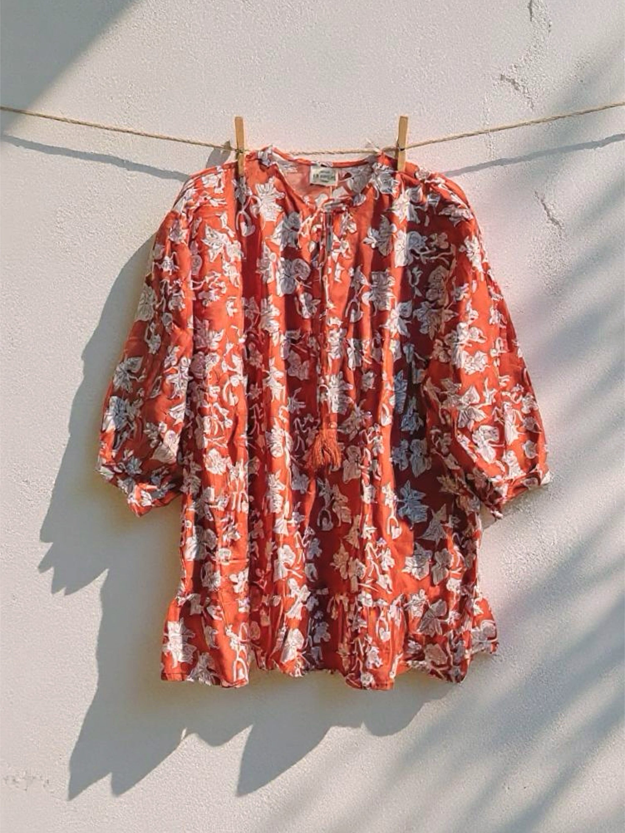 Change the picture to be a masterclass —captures a beautifully minimal and sun-soaked moment—this exact top, effortlessly hanging from a clothesline against a white rough textured wall. The soft shadows cast by the afternoon light add depth and movement, evoking a relaxed, nostalgic summer vibe. It’s raw and natural yet curated—reminiscent of vintage film photography. The photo style should be surreal, photorealistic.