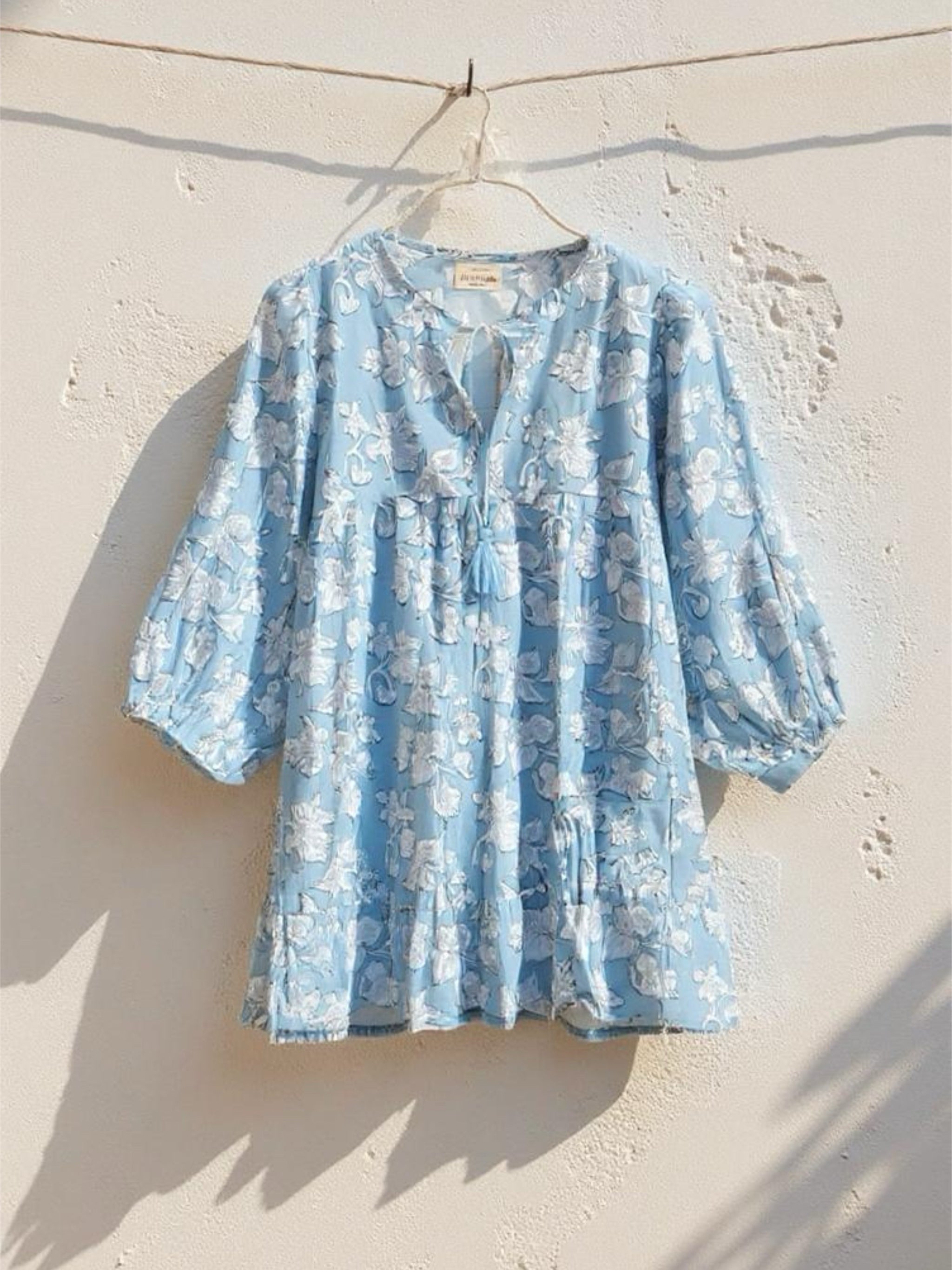Change the picture to be a masterclass —captures a beautifully minimal and sun-soaked moment—this exact top, effortlessly hanging from a clothesline against a white rough textured wall. The soft shadows cast by the afternoon light add depth and movement, evoking a relaxed, nostalgic summer vibe. It’s raw and natural yet curated—reminiscent of vintage film photography. The photo style should be surreal, photorealistic.