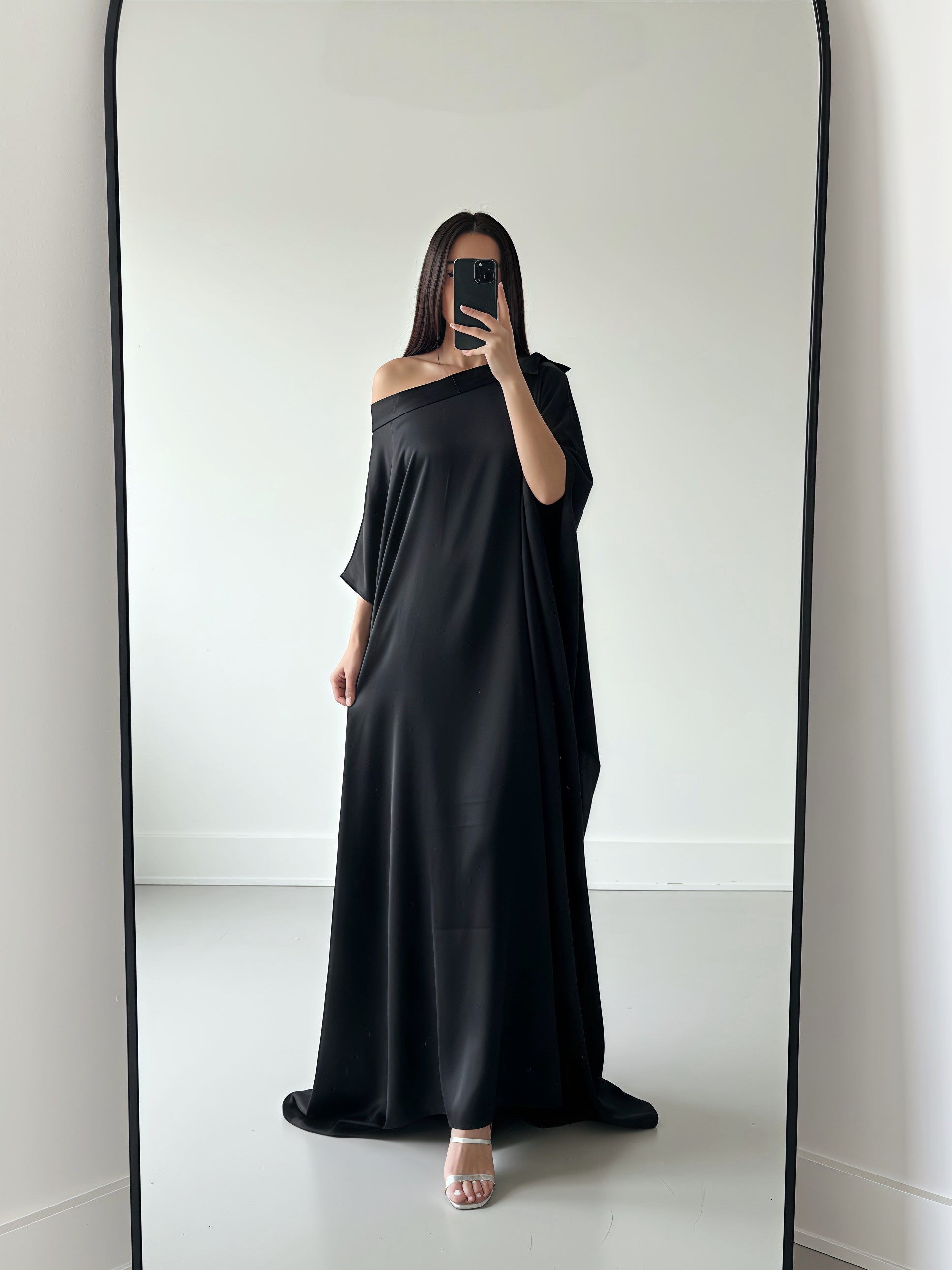 Person wearing a black off-shoulder kaftan dress standing in front of a mirror.