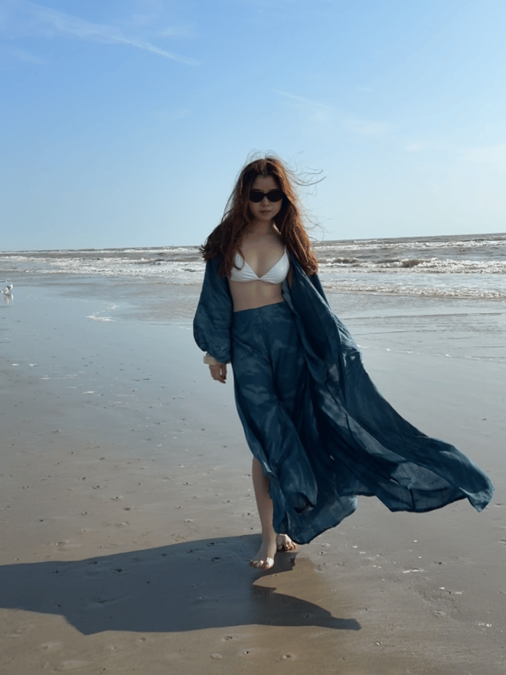 Woman wearing a long teal seashell tie dye kimono robe over a white bikini on the beach – boho beach cover up and vacation resort wear by Coco De Chom.