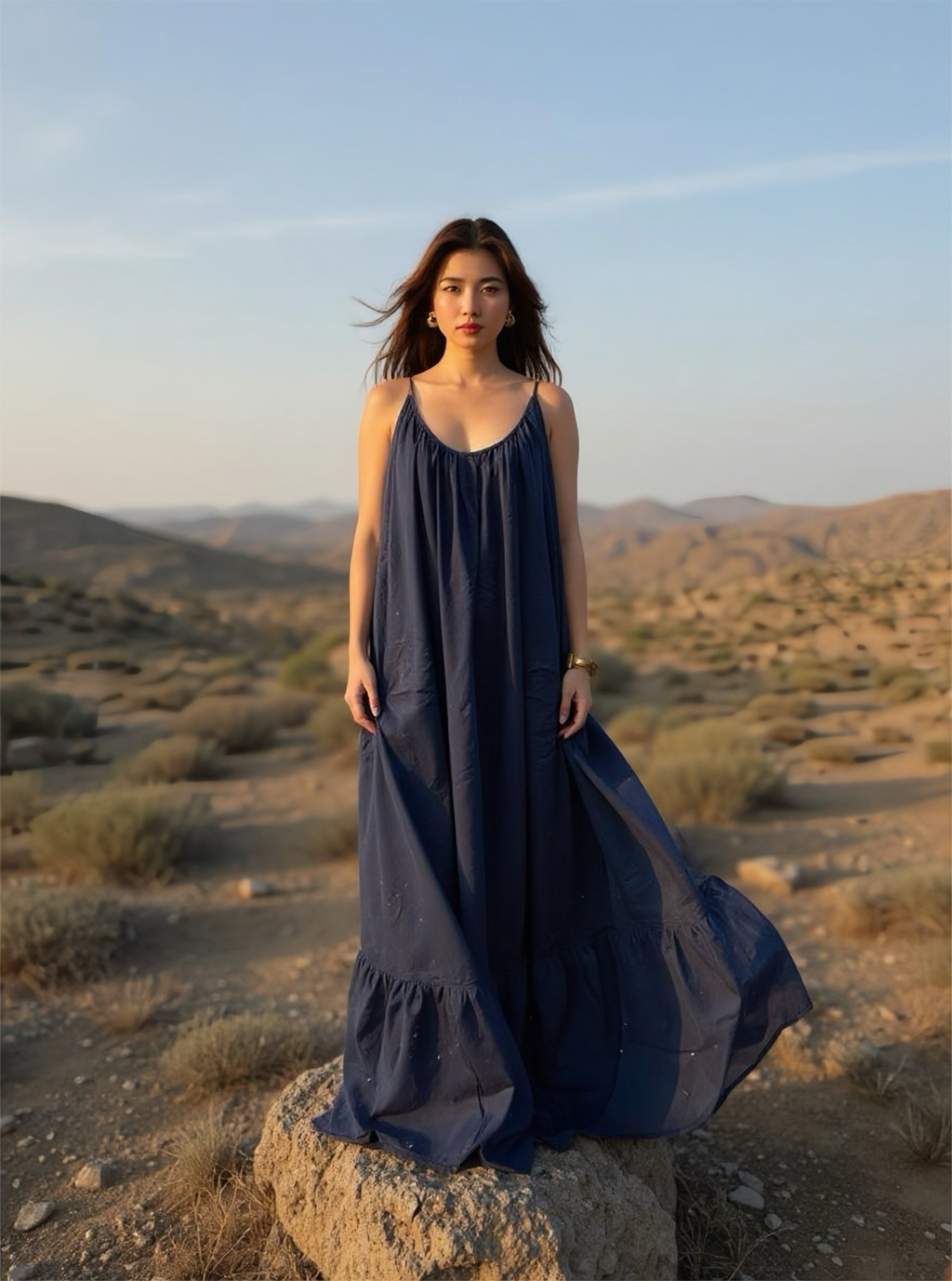 Model in navy backless maxi dress with flowing fit, posing outdoors in a desert mountain landscape.