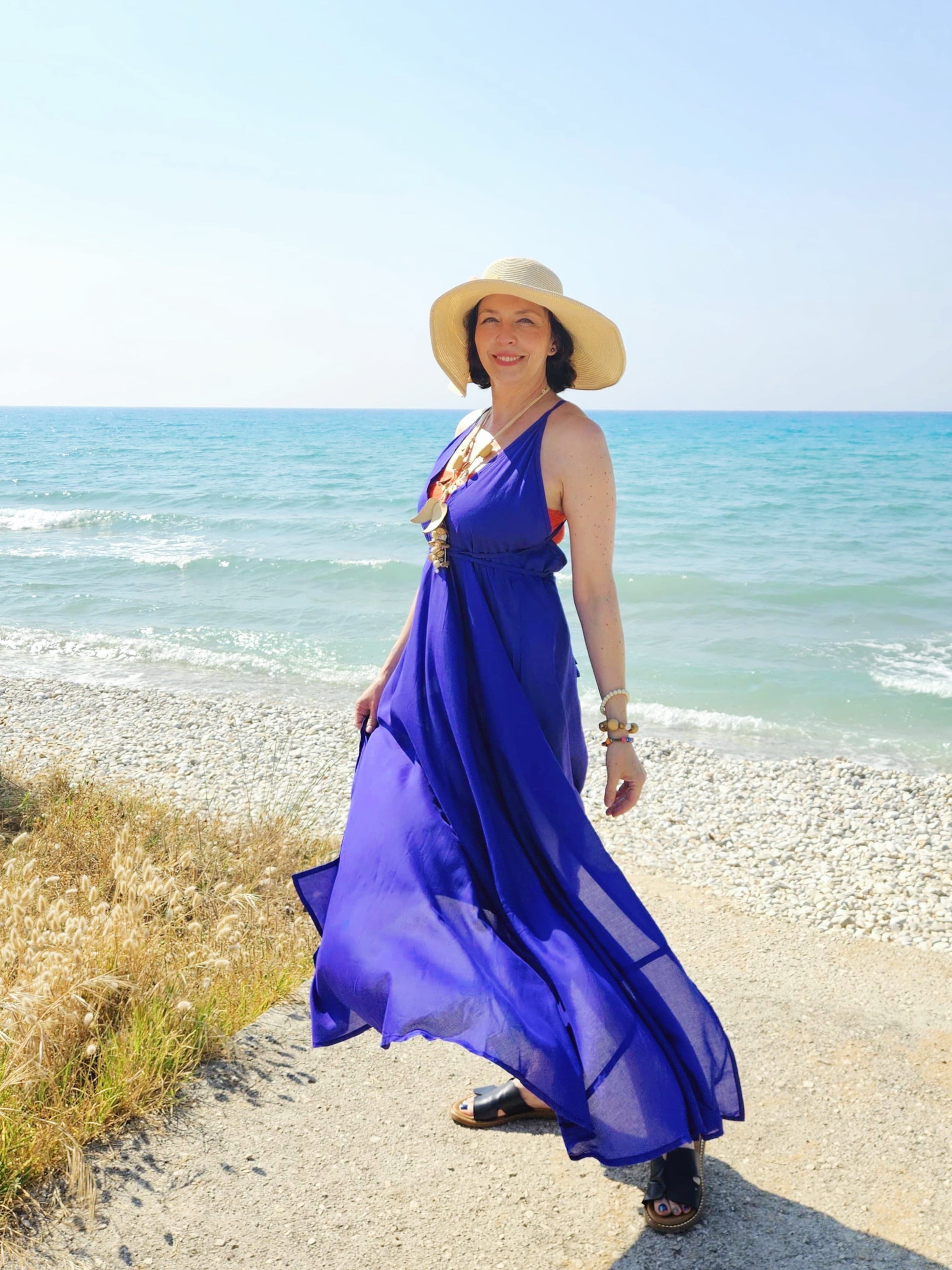 Woman wearing a flowy, hand-dyed purple blue halter maxi dress with open back and high slit, styled as beachy resort wear, perfect beach dress under an arched walkway.
