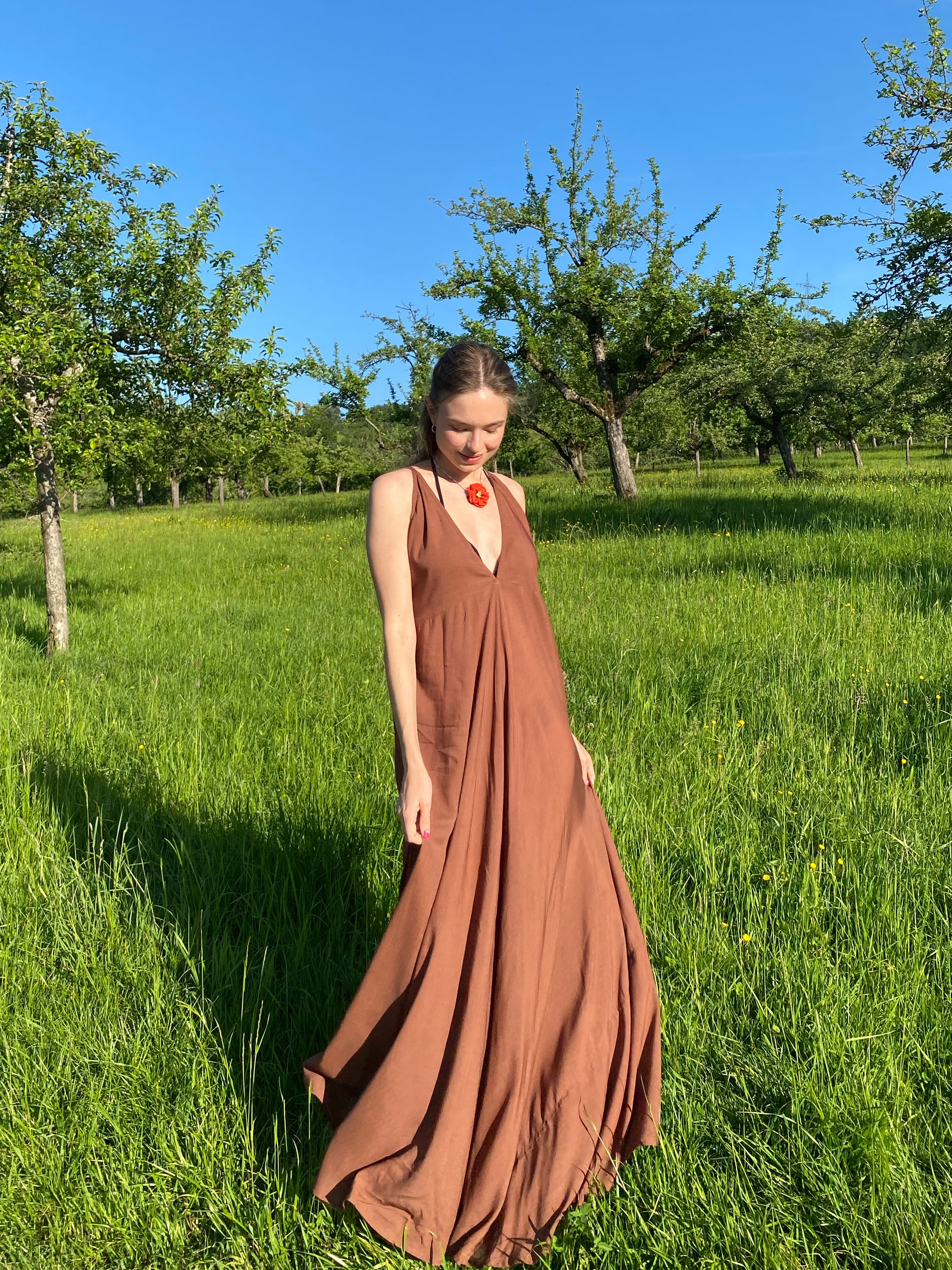 Woman wearing a flowy, hand-dyed brown halter maxi dress with open back and high slit, styled as boho stye resort wear under in the field.